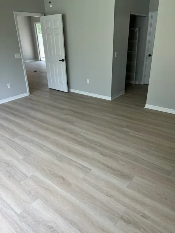Empty room with light wood-look flooring and gray walls. White door and trim are visible.