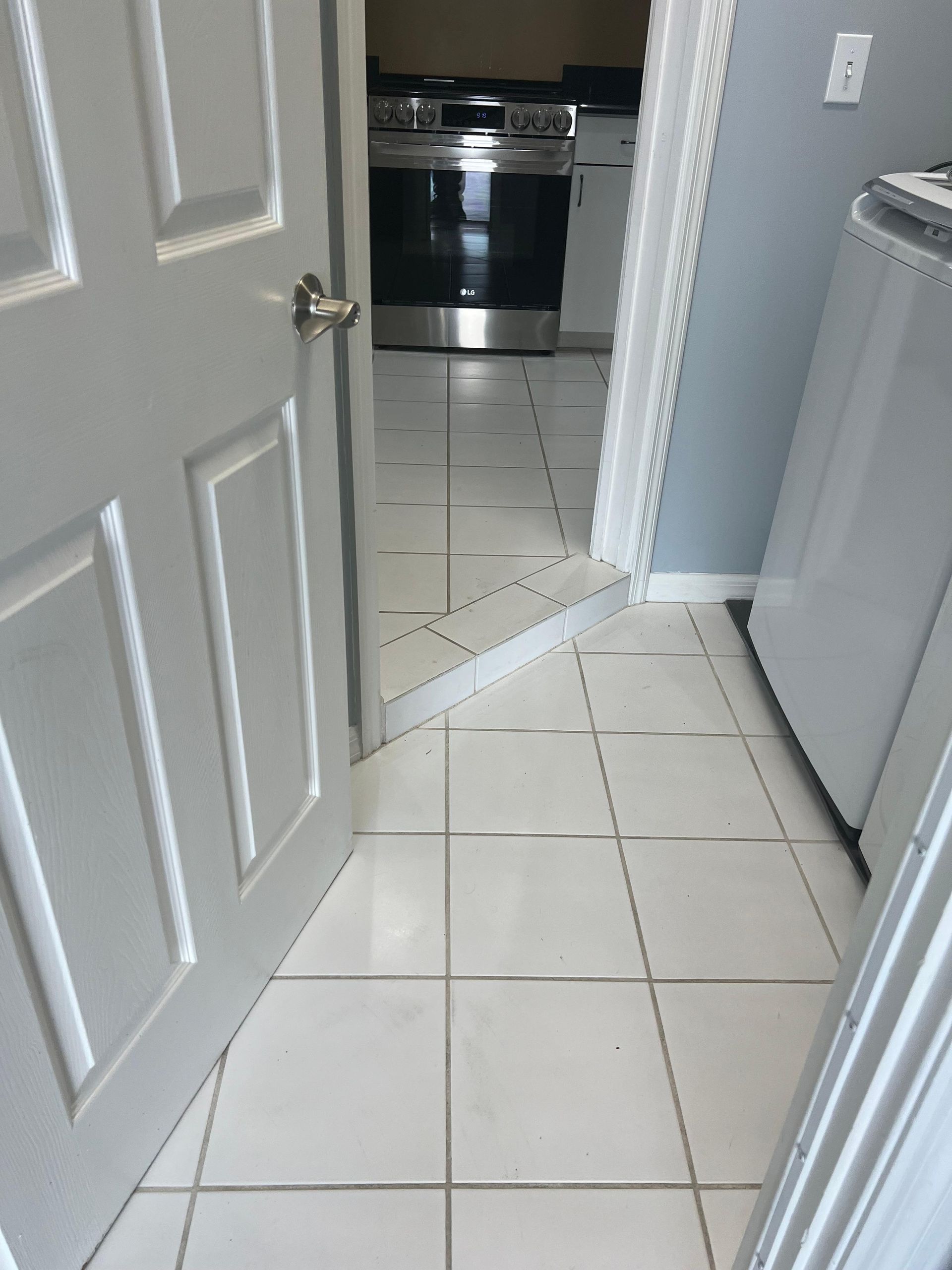 A white tiled floor leads to a kitchen with a stove and a washer and dryer