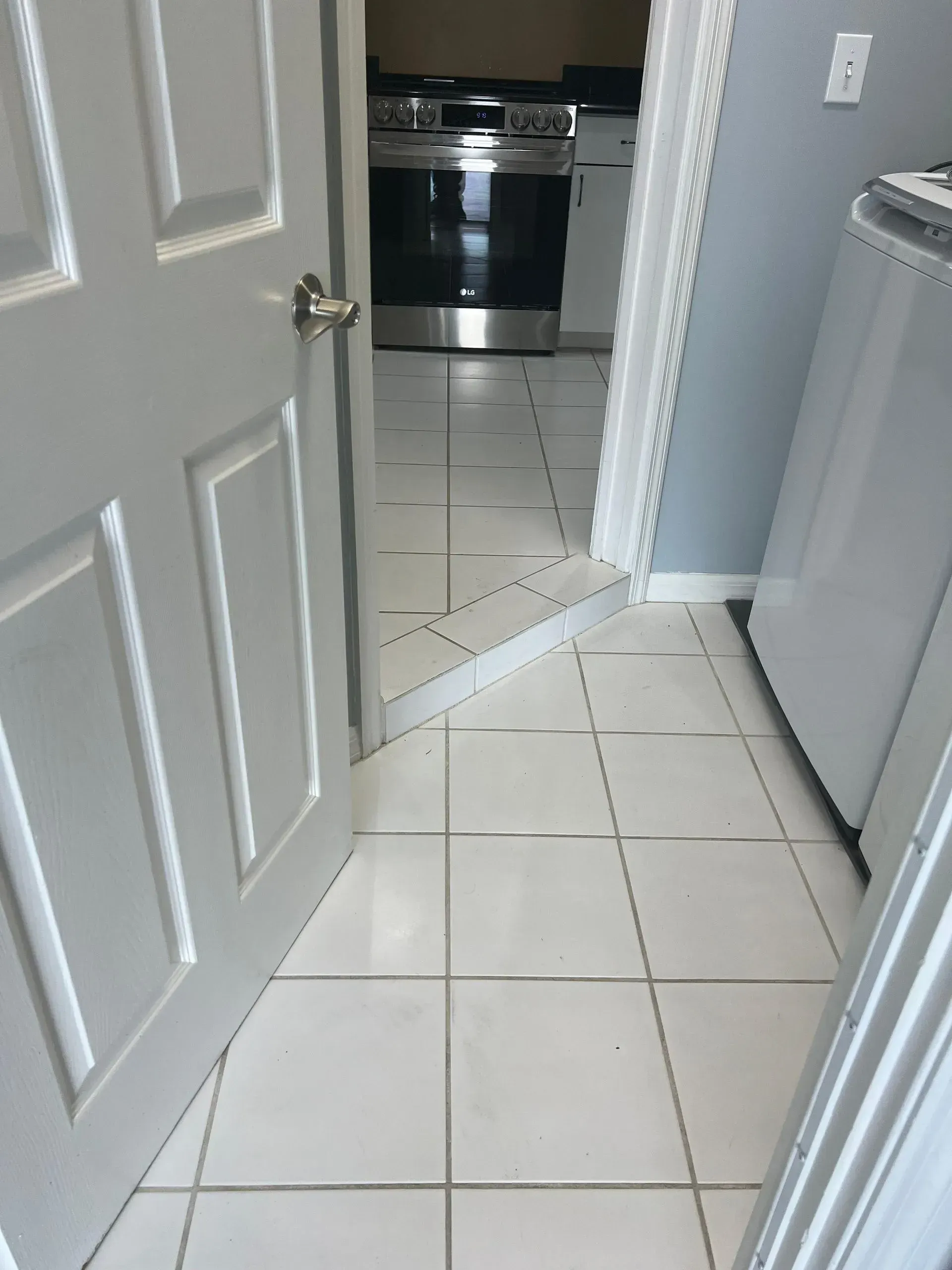 White tiled floor with a doorway leading to a kitchen with a stove visible.