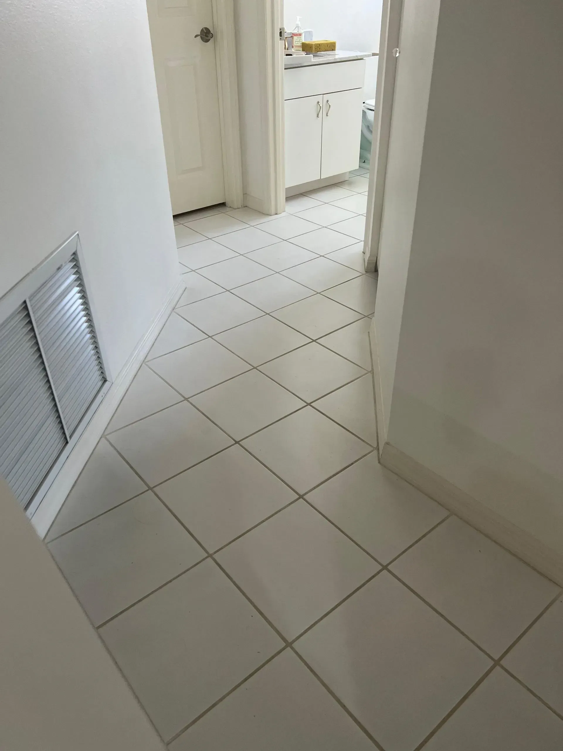 Hallway with white tile flooring leading to a bathroom, white walls and a white door.
