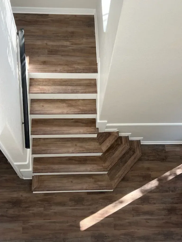 Wooden staircase with white trim, viewed from above, bathed in sunlight.