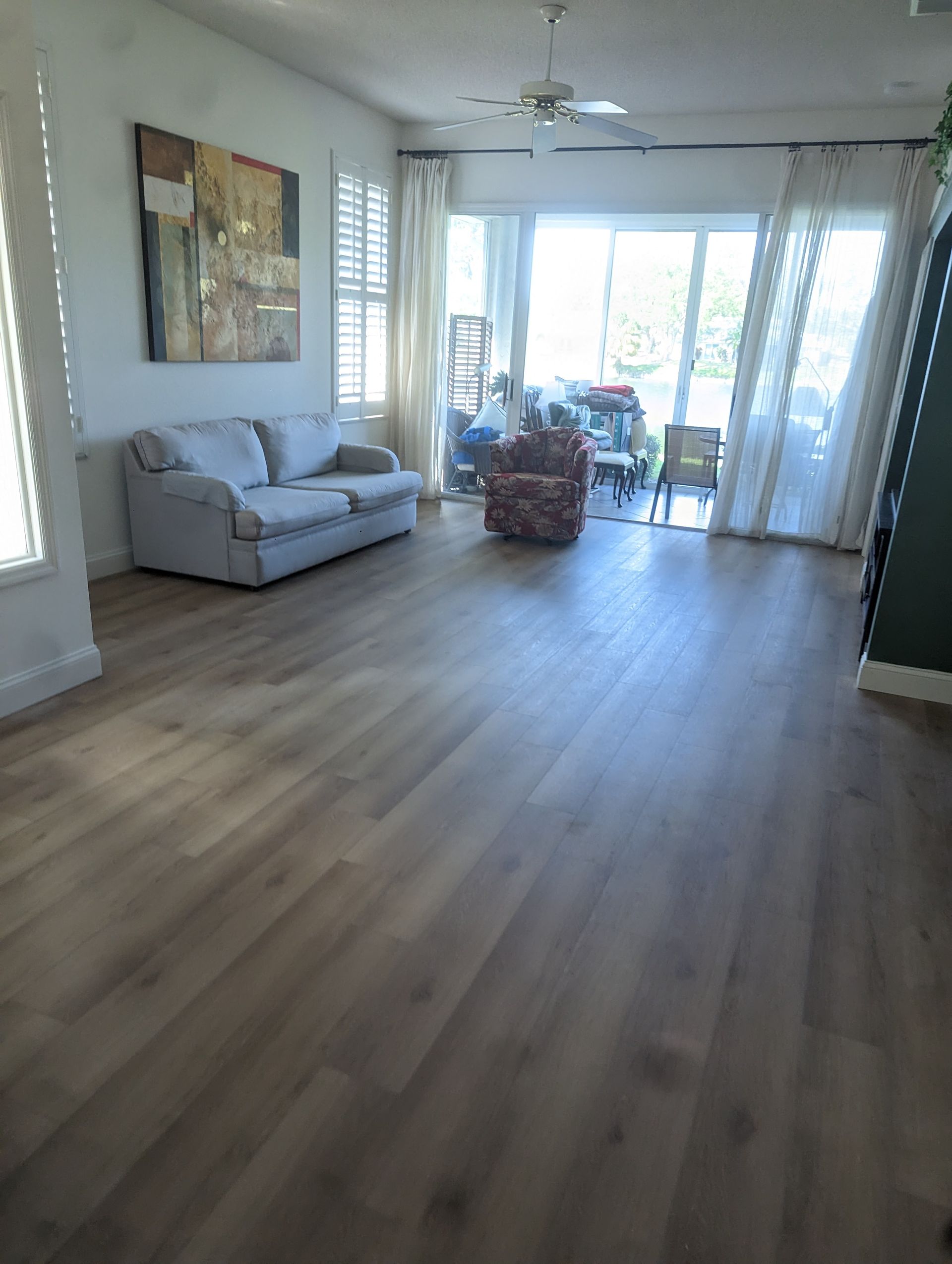 A living room with hardwood floors , a couch , chairs and a painting on the wall.