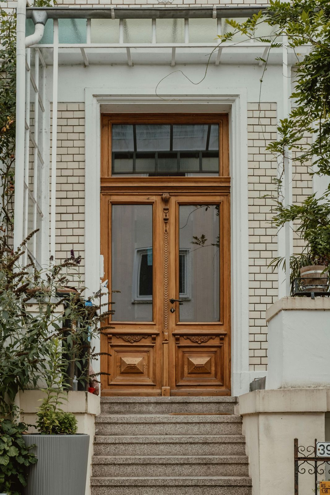 Wooden double doors with glass panels and a transom window above, set in a light brick facade.
