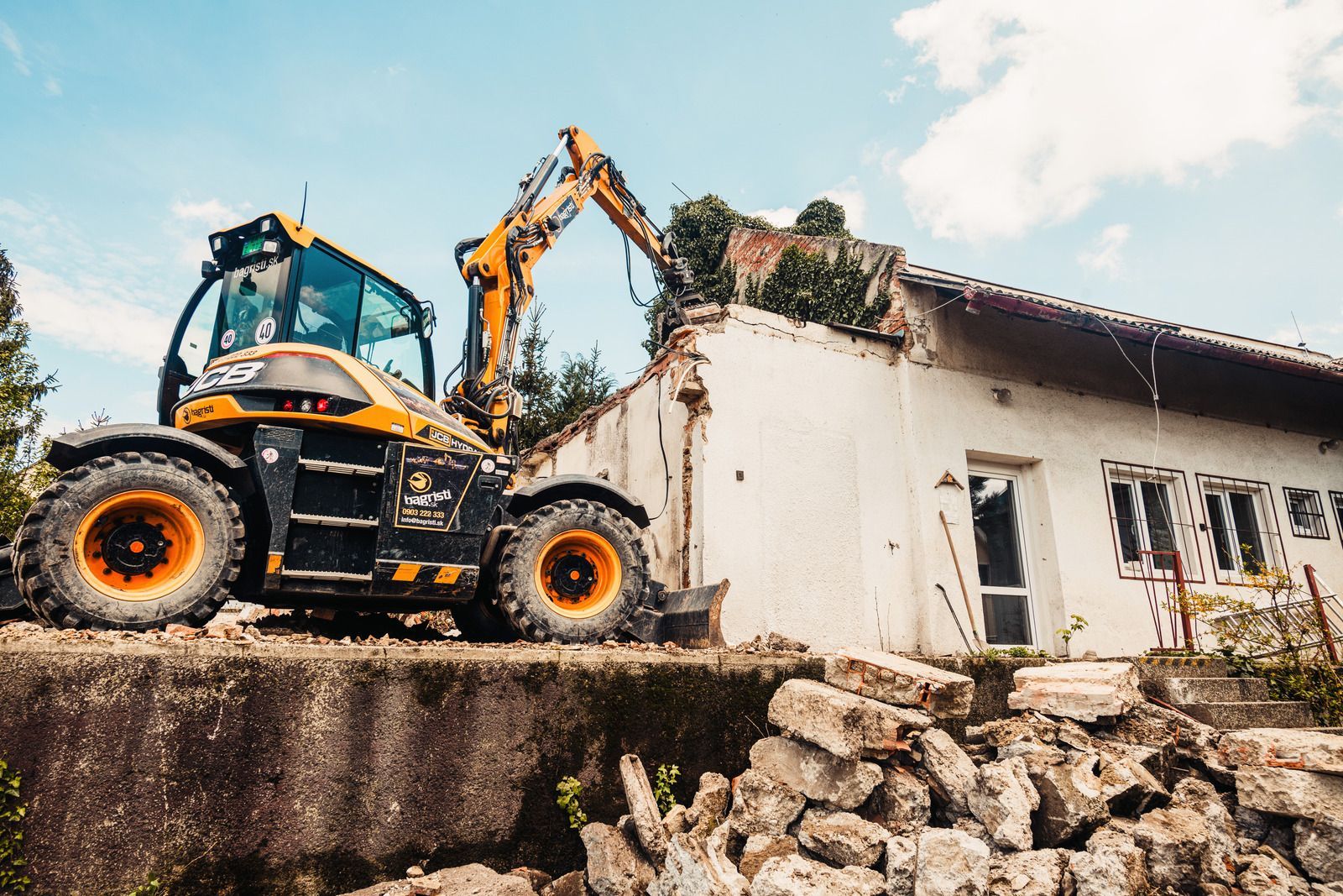 Yellow excavator demolishing a white building, debris on the ground.