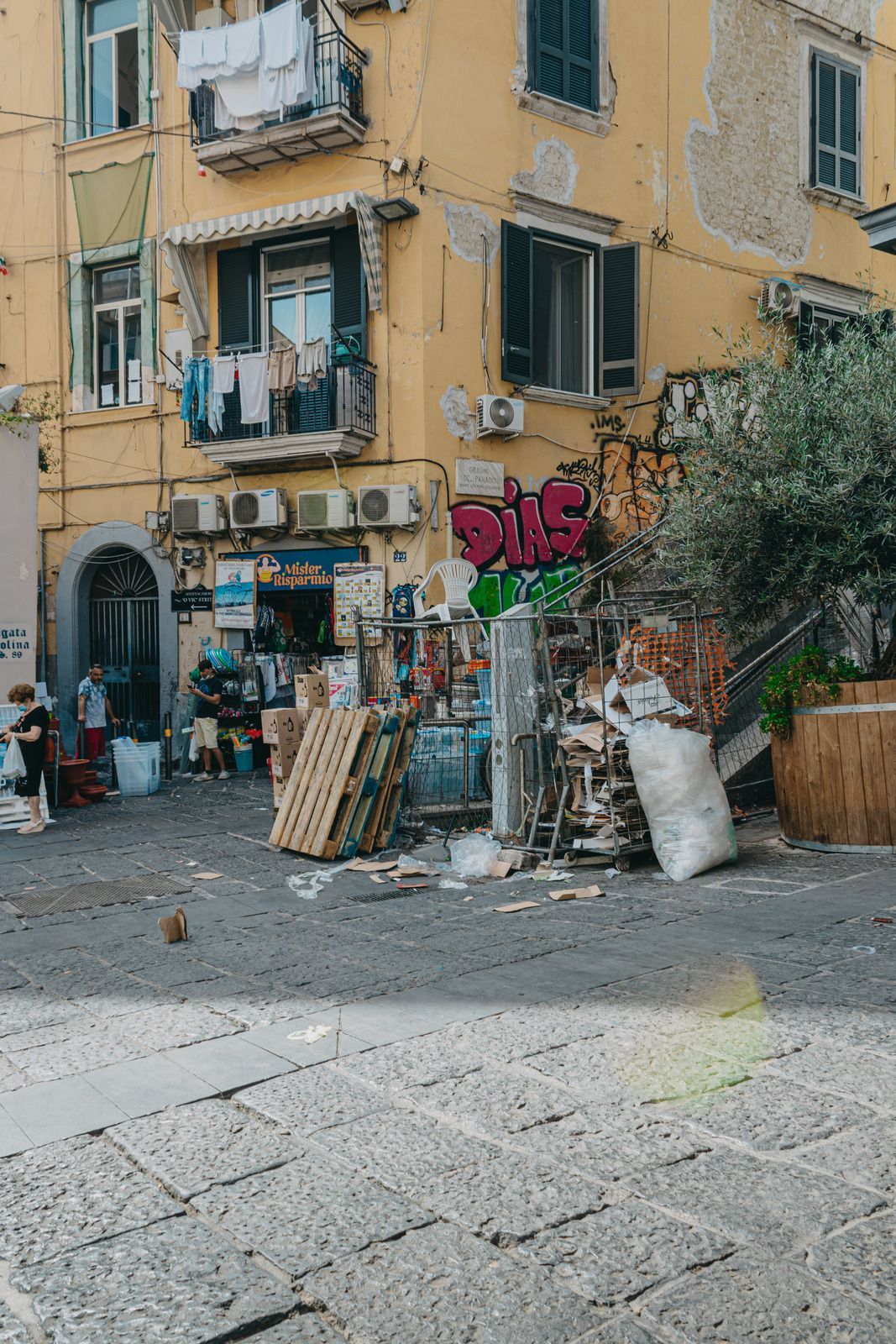 Yellow building with open windows and laundry, shopfront, pallets, and graffiti.
