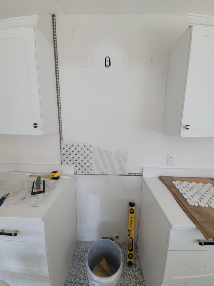 A kitchen with white cabinets , a bucket , a level , and a tape measure.