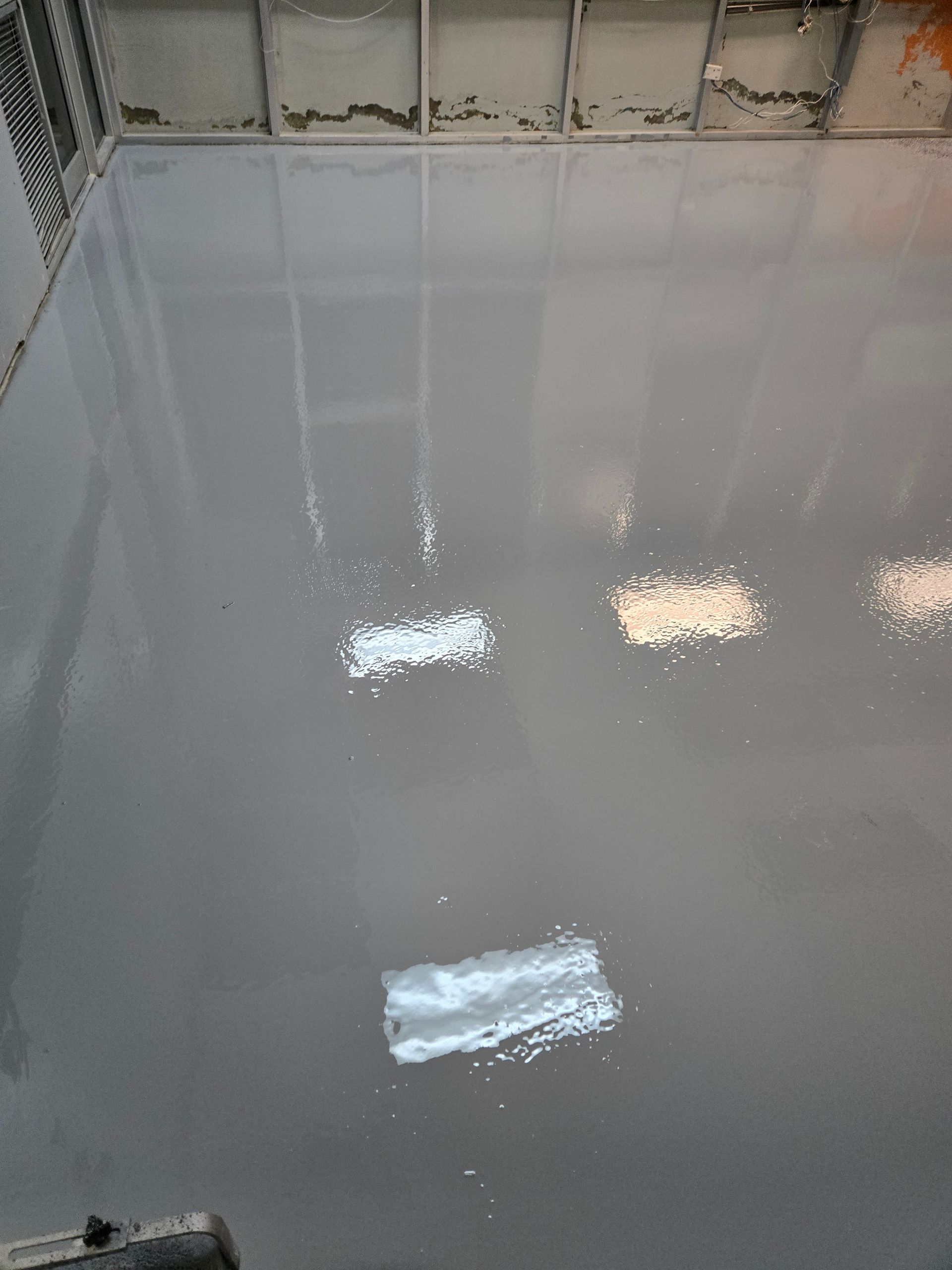 Woman in green uniform smiles, pushing cleaning cart in modern building hallway.