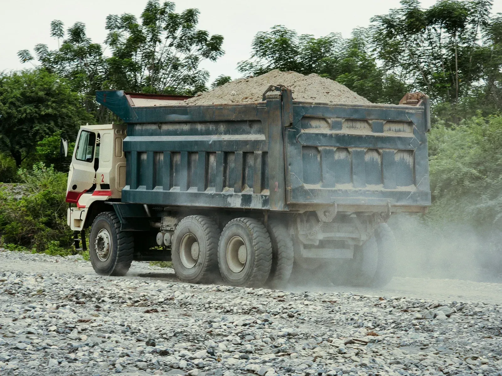 Dump truck hauling gravel on a dusty road.