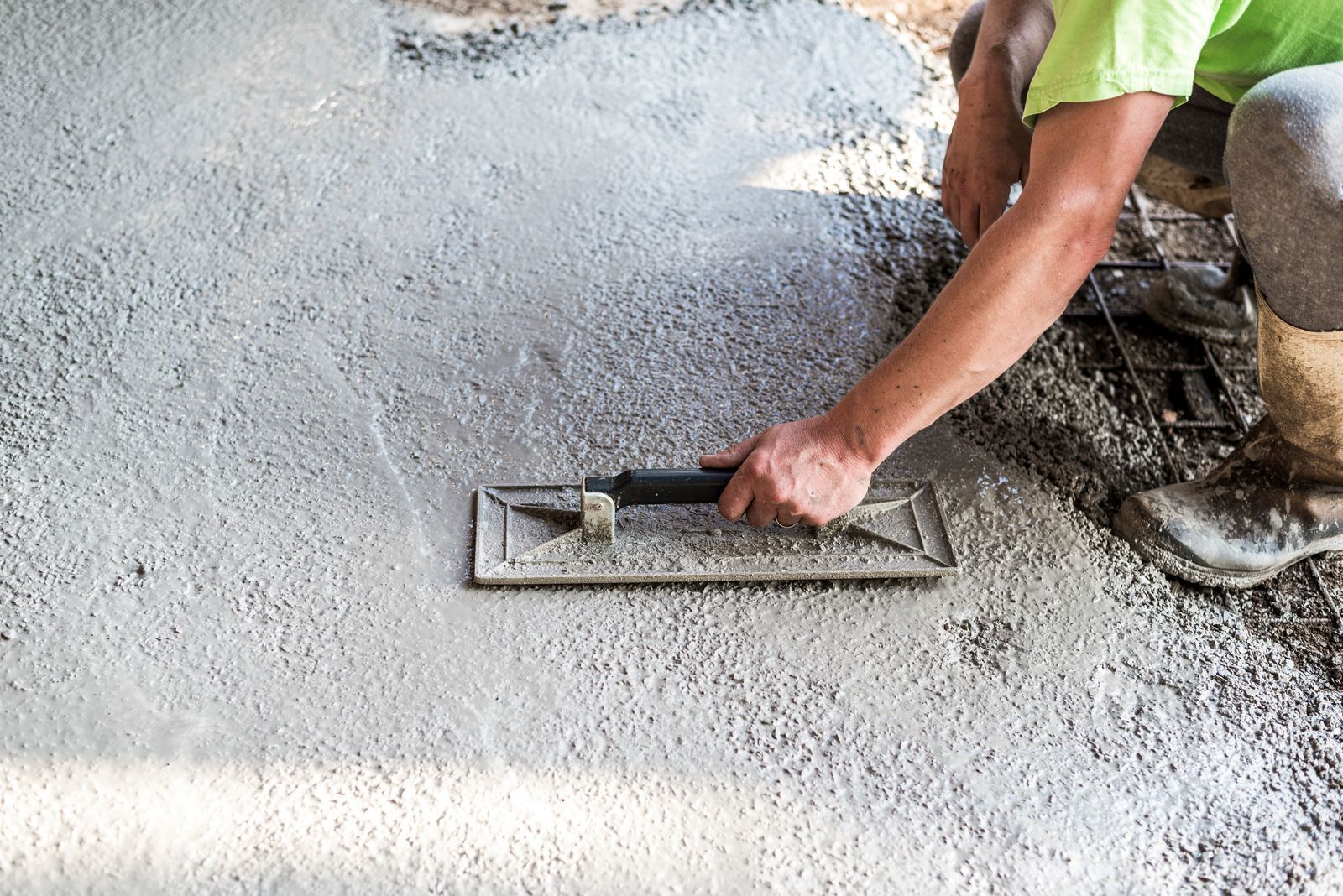 Person smoothing wet concrete with a trowel, outdoors.
