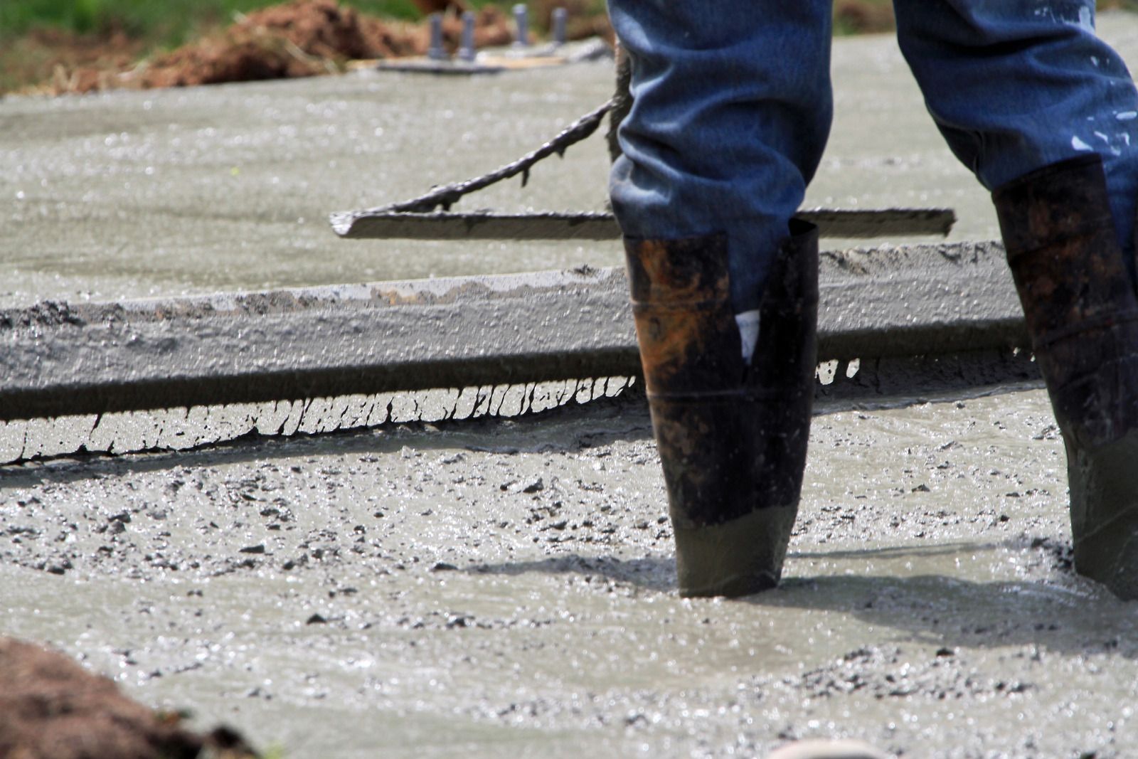 Person in boots screeds wet concrete with a tool.