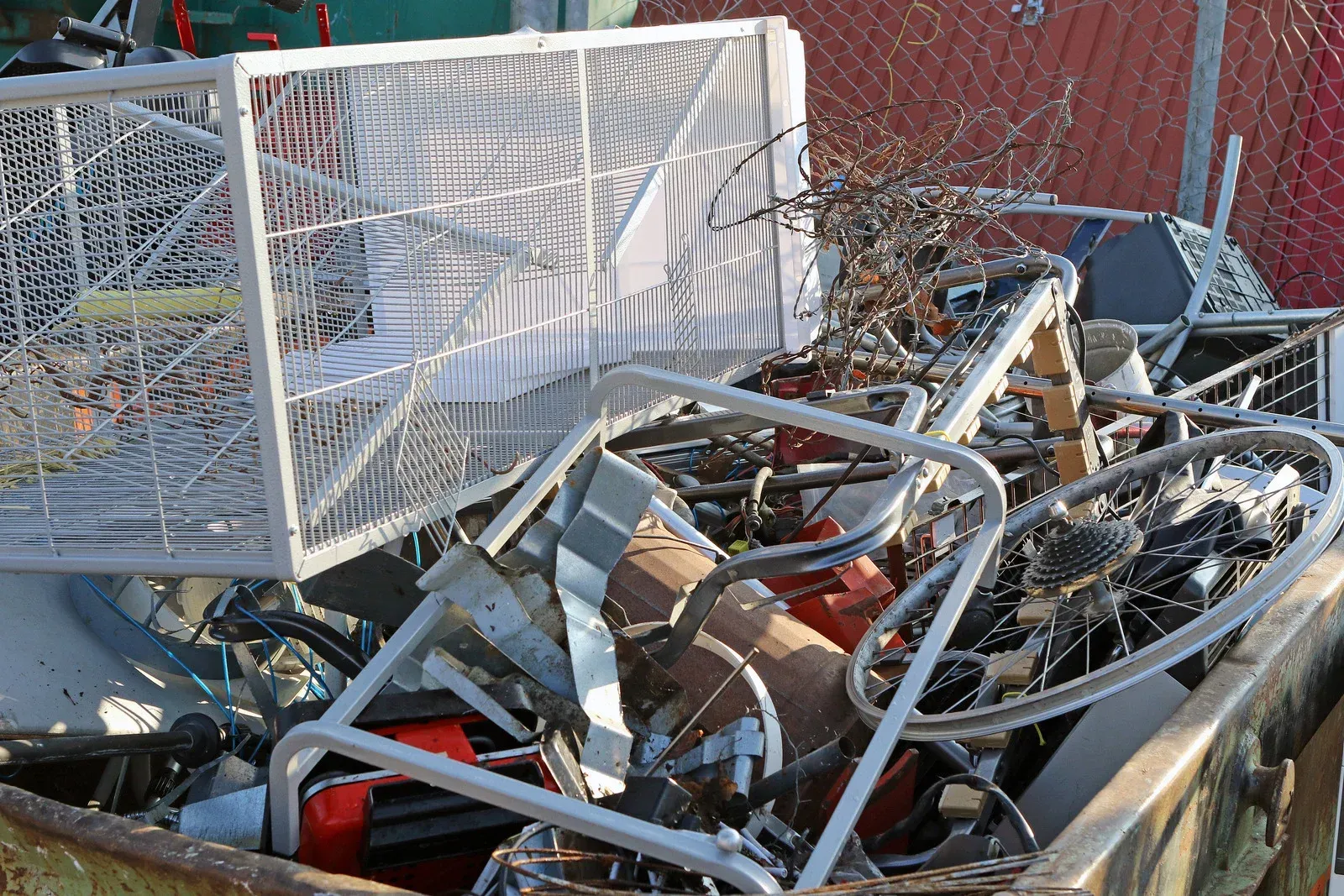 Scrap metal bin overflowing with various metal objects, including a shopping cart, bicycle parts.