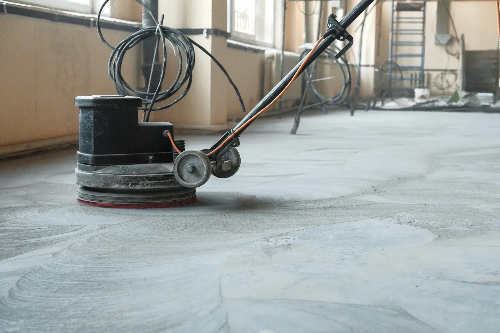 Floor sander cleaning a gray concrete floor in an industrial setting.