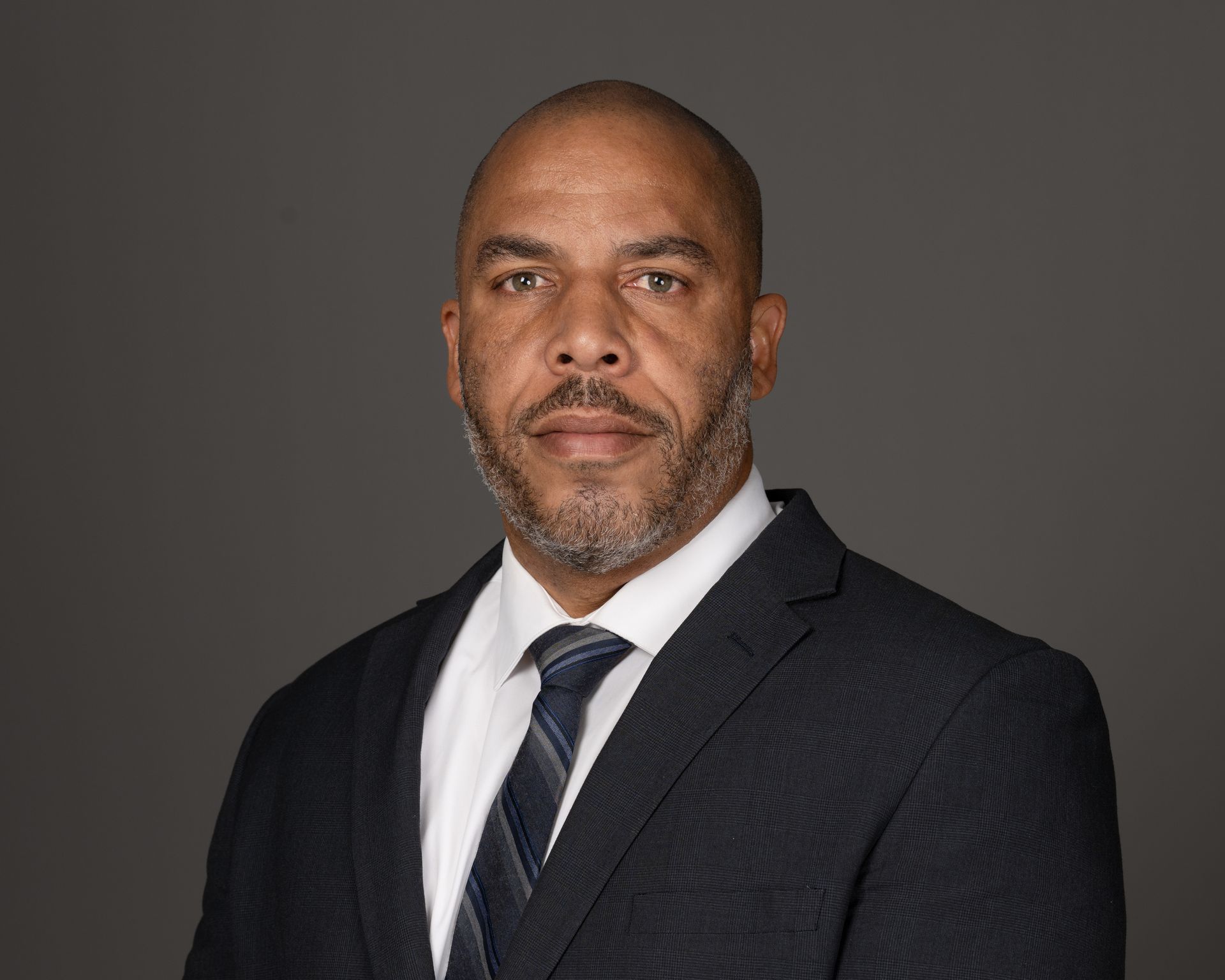 A man in a suit and tie is standing in front of a gray background.