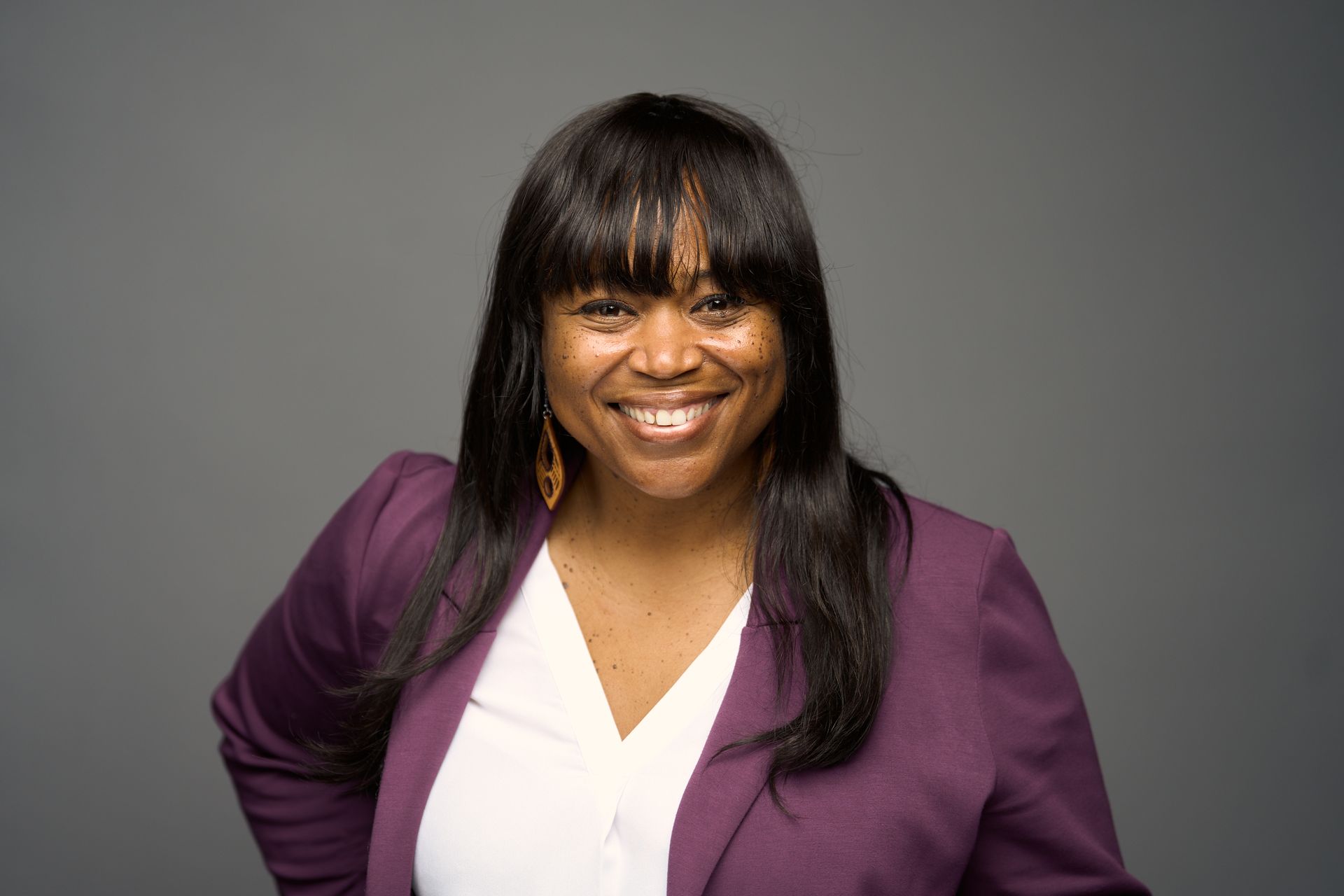A woman wearing a purple dress and a silver earrings is smiling for the camera.