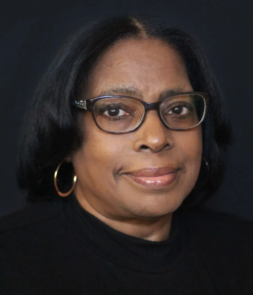 A woman wearing glasses and hoop earrings is smiling for the camera