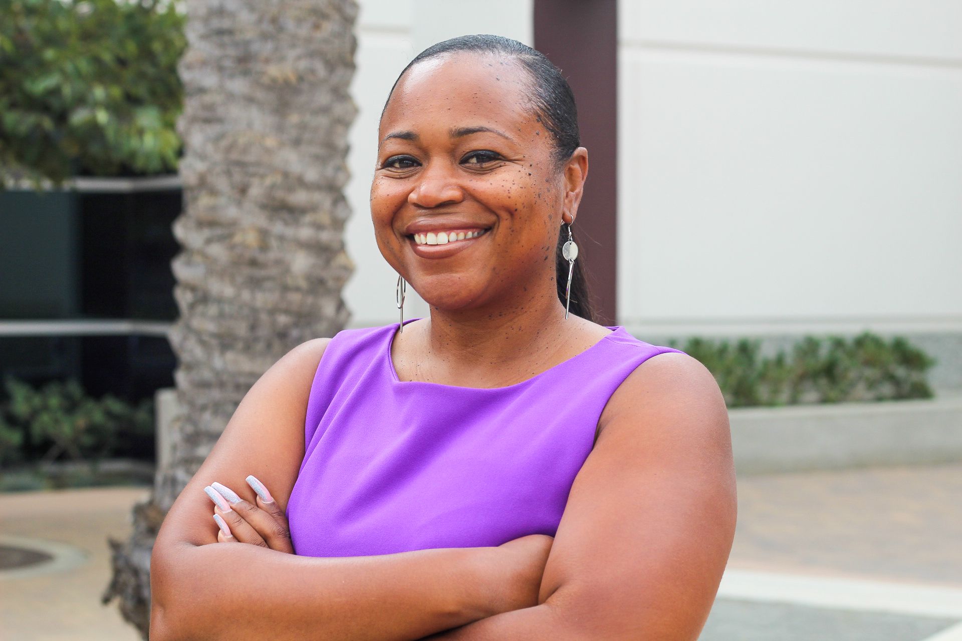 A woman wearing a purple dress and a silver earrings is smiling for the camera.