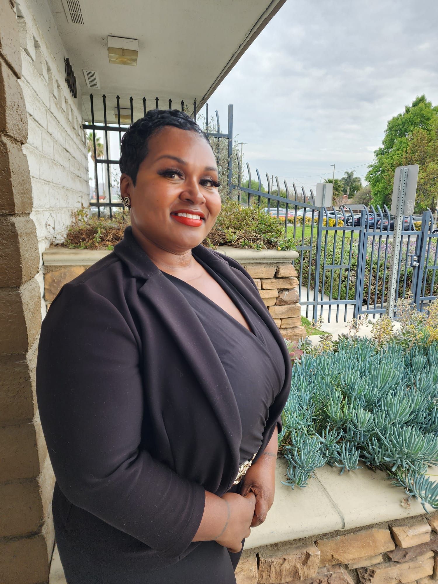 A woman in a black suit is standing in front of a building.
