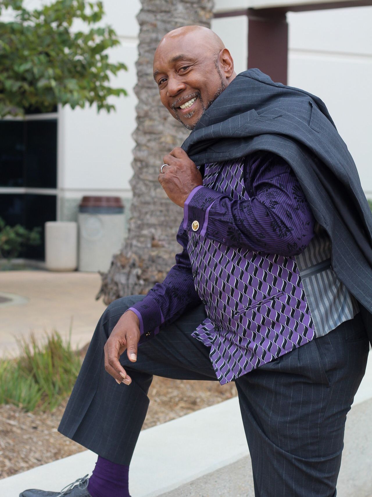 A man in a suit and purple vest is sitting on a wall.