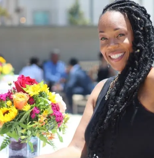 A woman is smiling while holding a vase of flowers