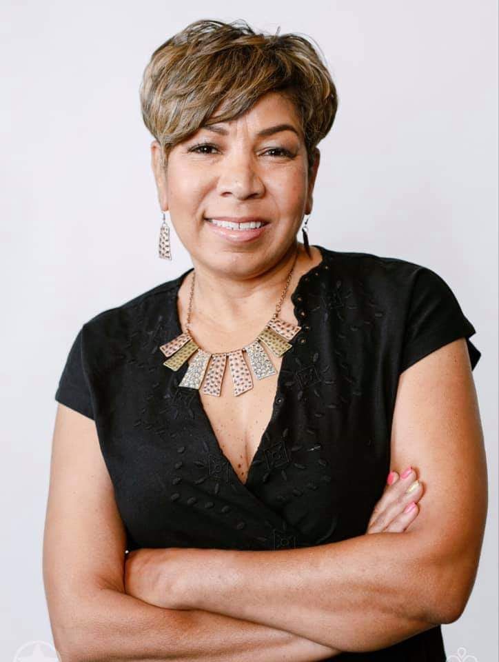A woman wearing a black shirt and a necklace is standing with her arms crossed.