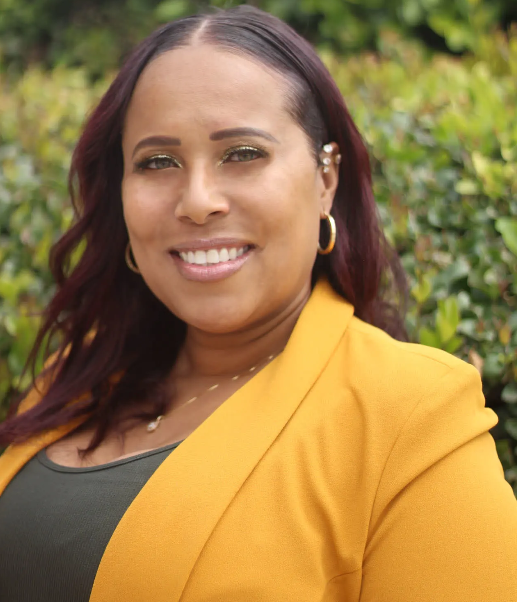 A woman wearing a yellow jacket and earrings is smiling for the camera.