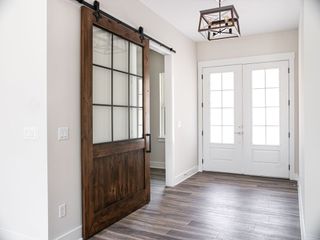 A wood barn-style door with glass panels opens into a hallway with white walls, wood floors, and double white entry doors.