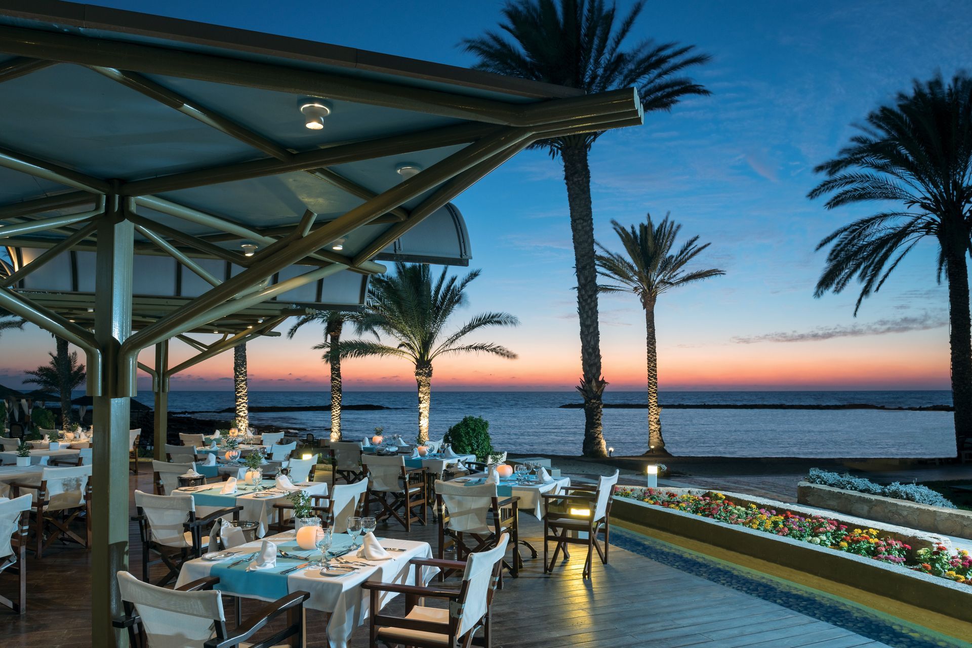 TUI Blue Pioneer Beach Hotel A restaurant with tables and chairs overlooking the ocean at sunset.