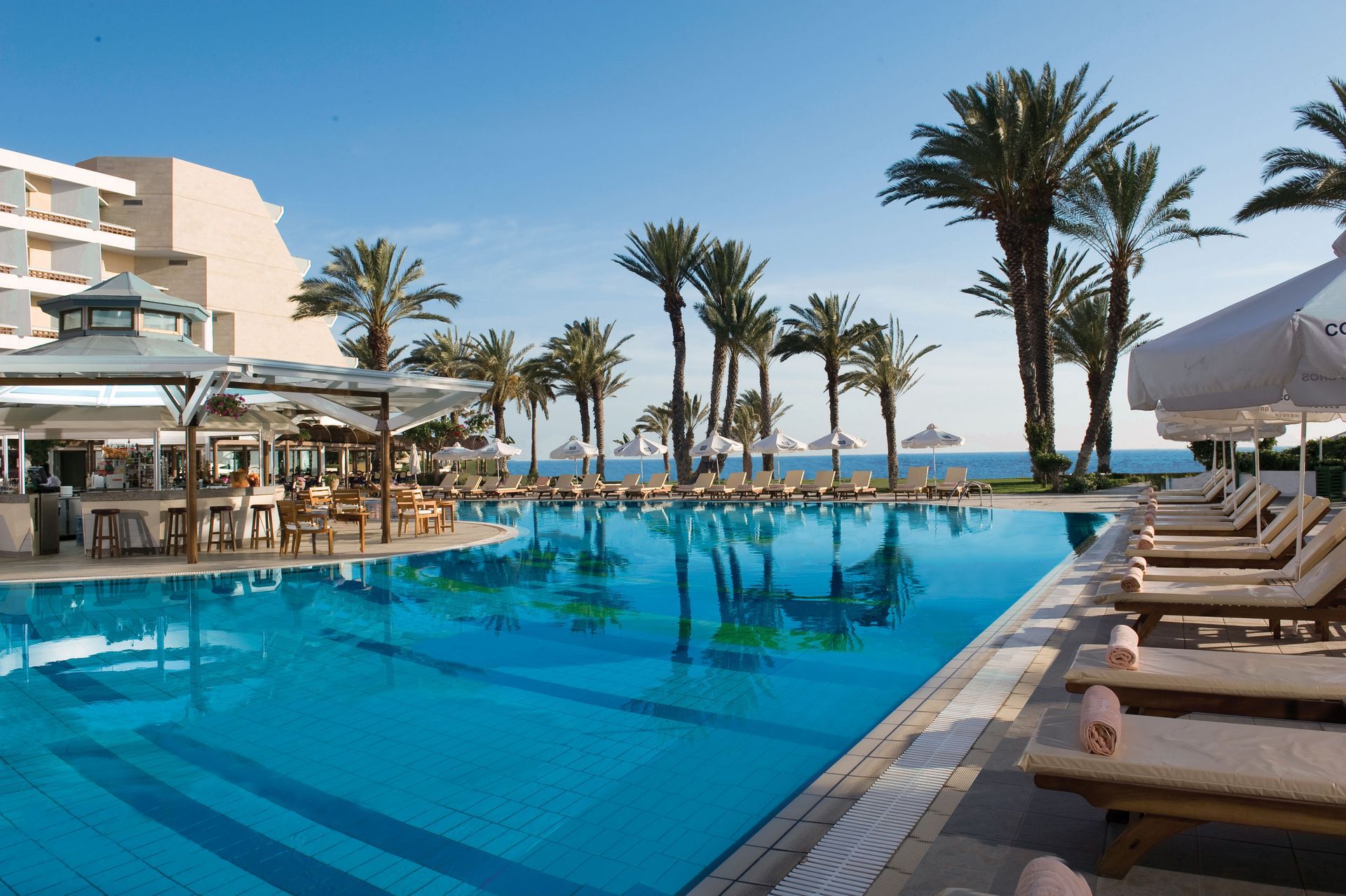 Constantinou Bros Hotels A large swimming pool surrounded by chairs and palm trees