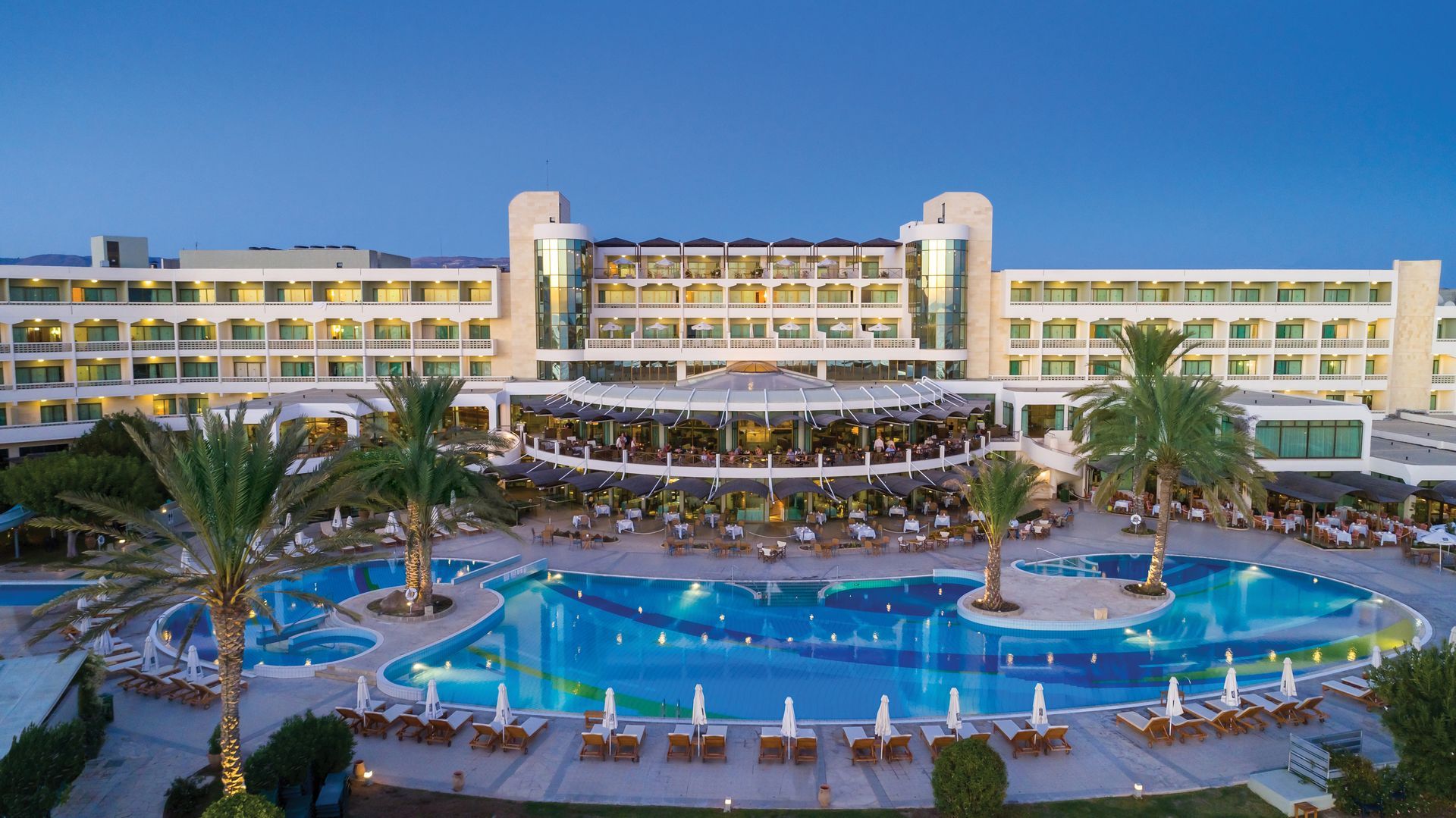 A large hotel with a large swimming pool in front of it.