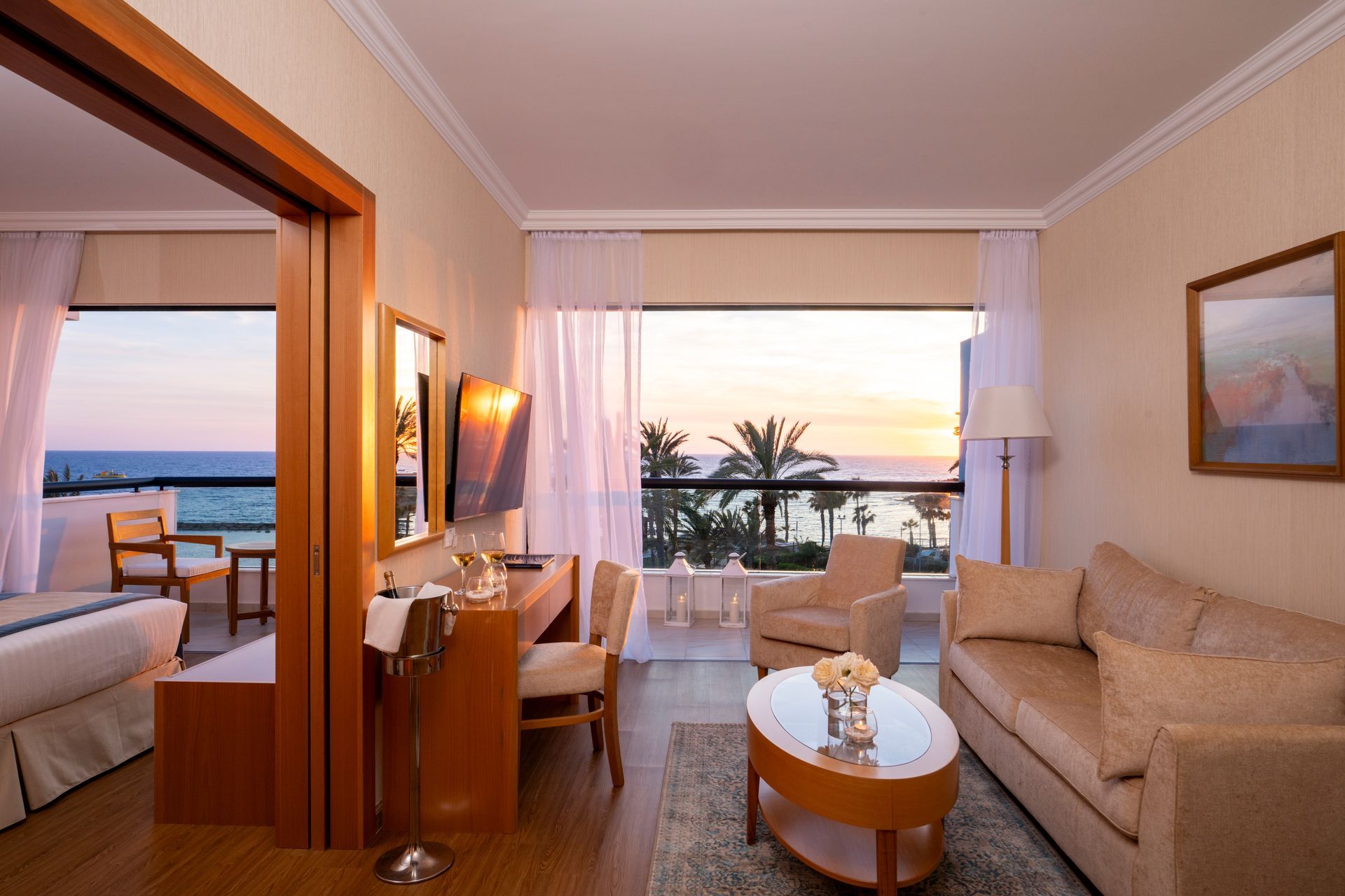 Cozy seaside hotel suite with sofa, desk, bed, and balcony view at sunset