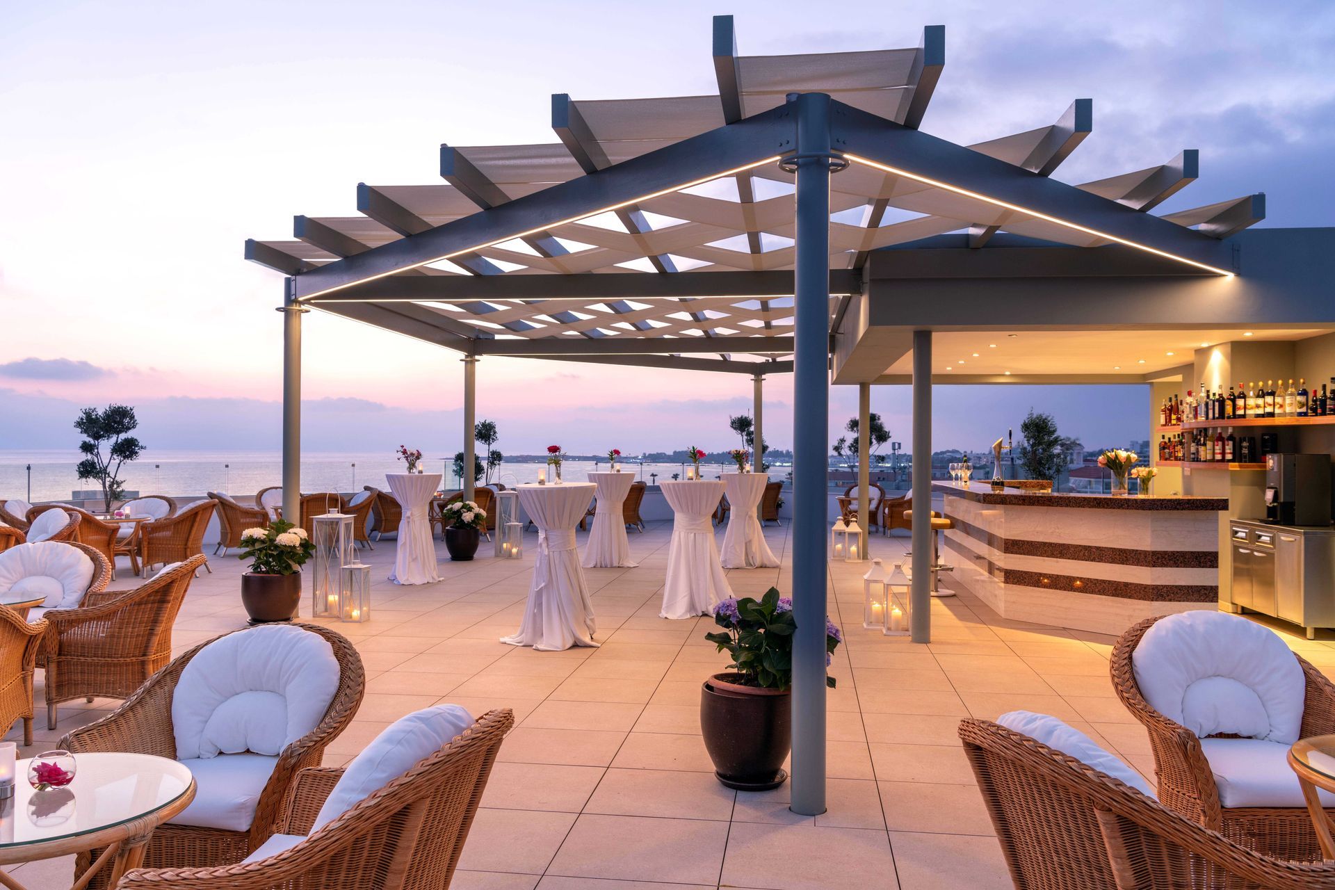 Athena Royal Beach Hotel A rooftop bar with tables and chairs and a pergola overlooking the ocean.