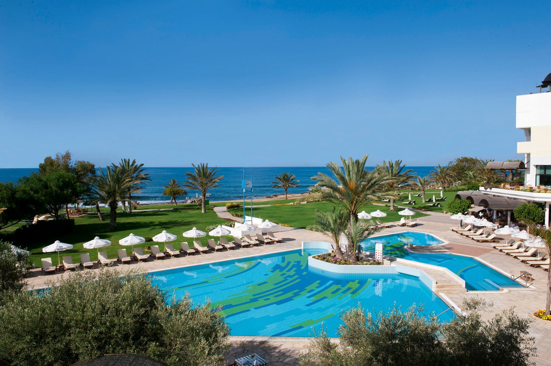 Constantinou Bros Hotels A large swimming pool surrounded by chairs and umbrellas next to the ocean.