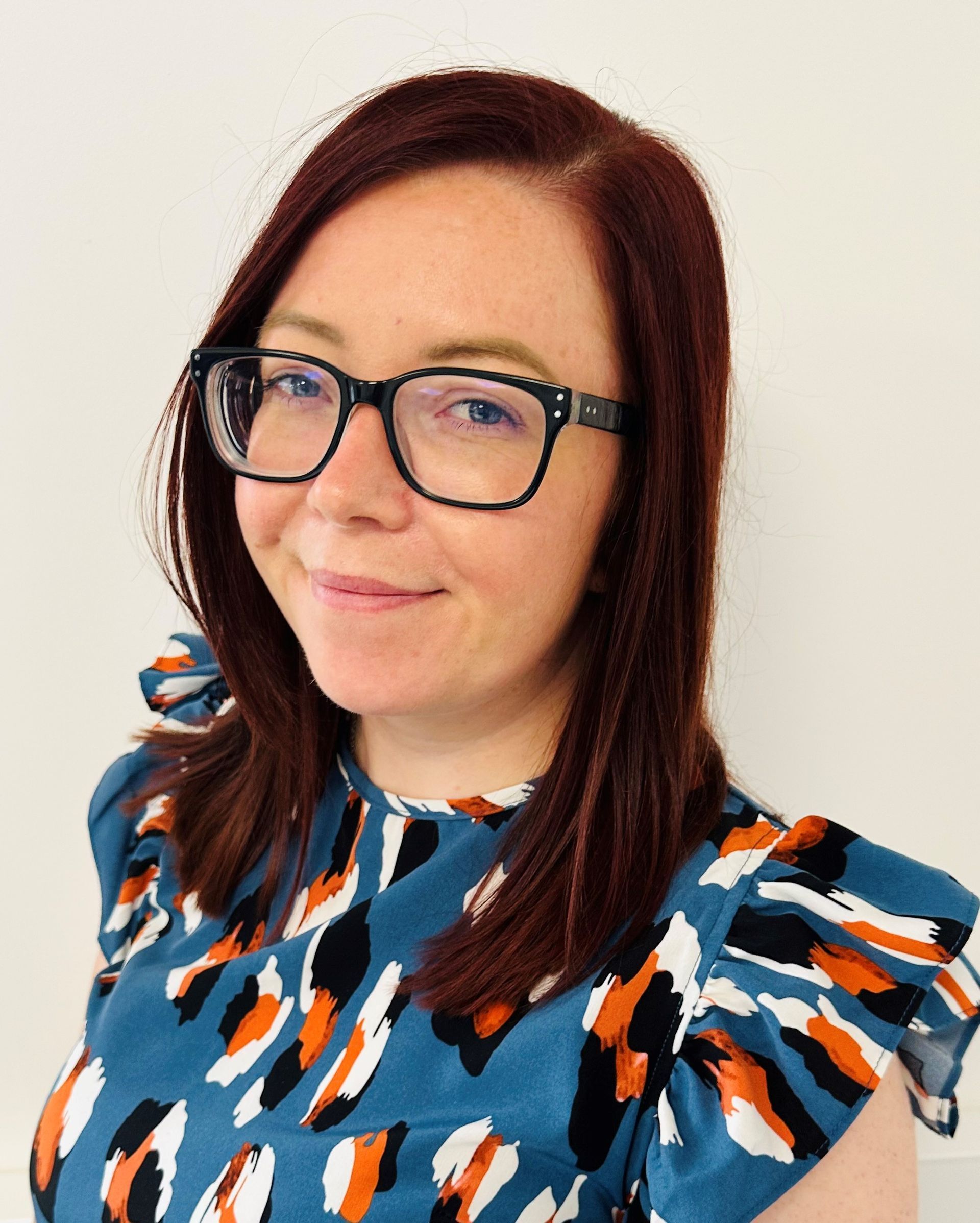 A woman wearing glasses and a blue shirt is smiling for the camera.