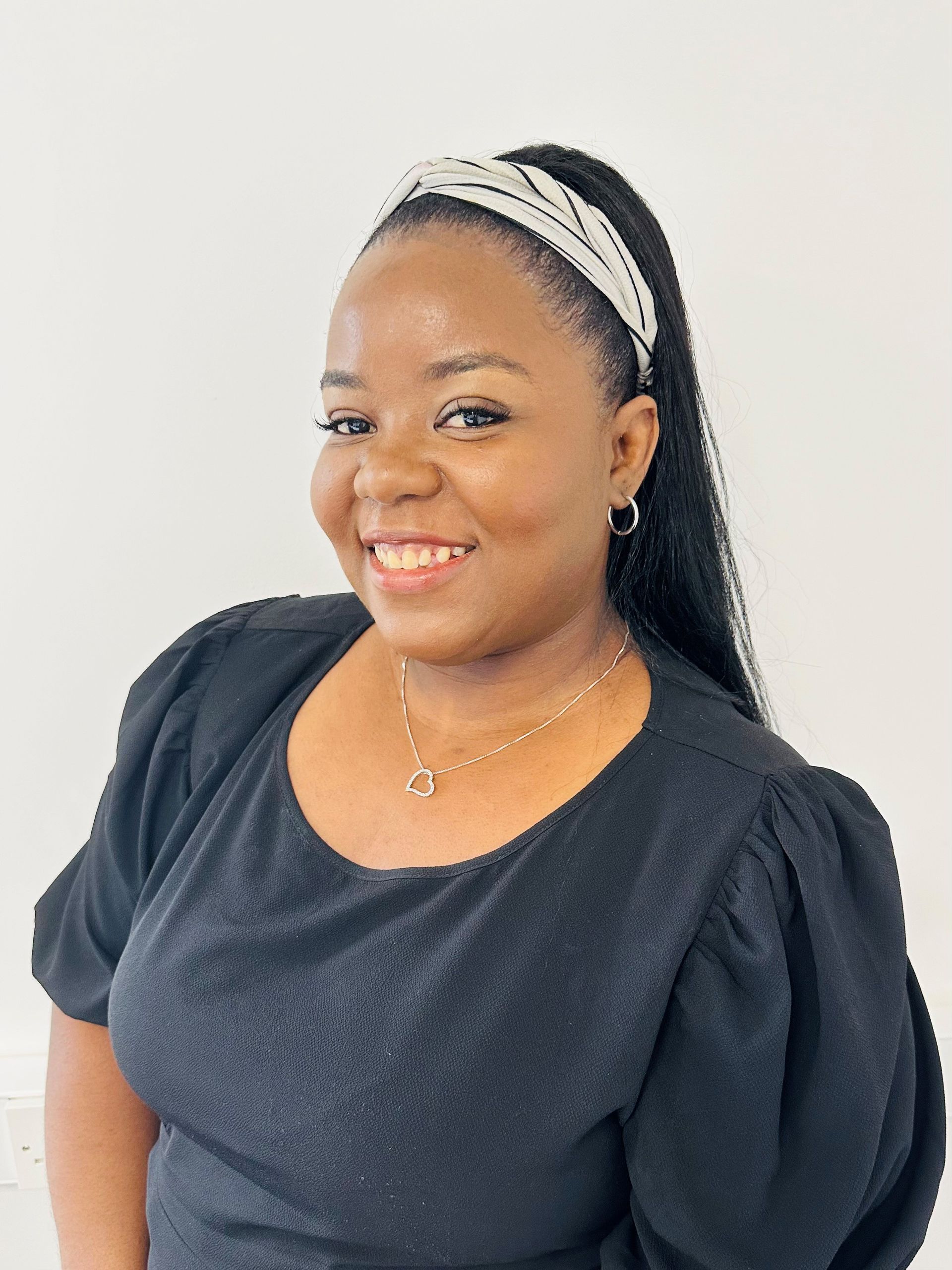 A woman wearing a black dress and a headband is smiling for the camera.