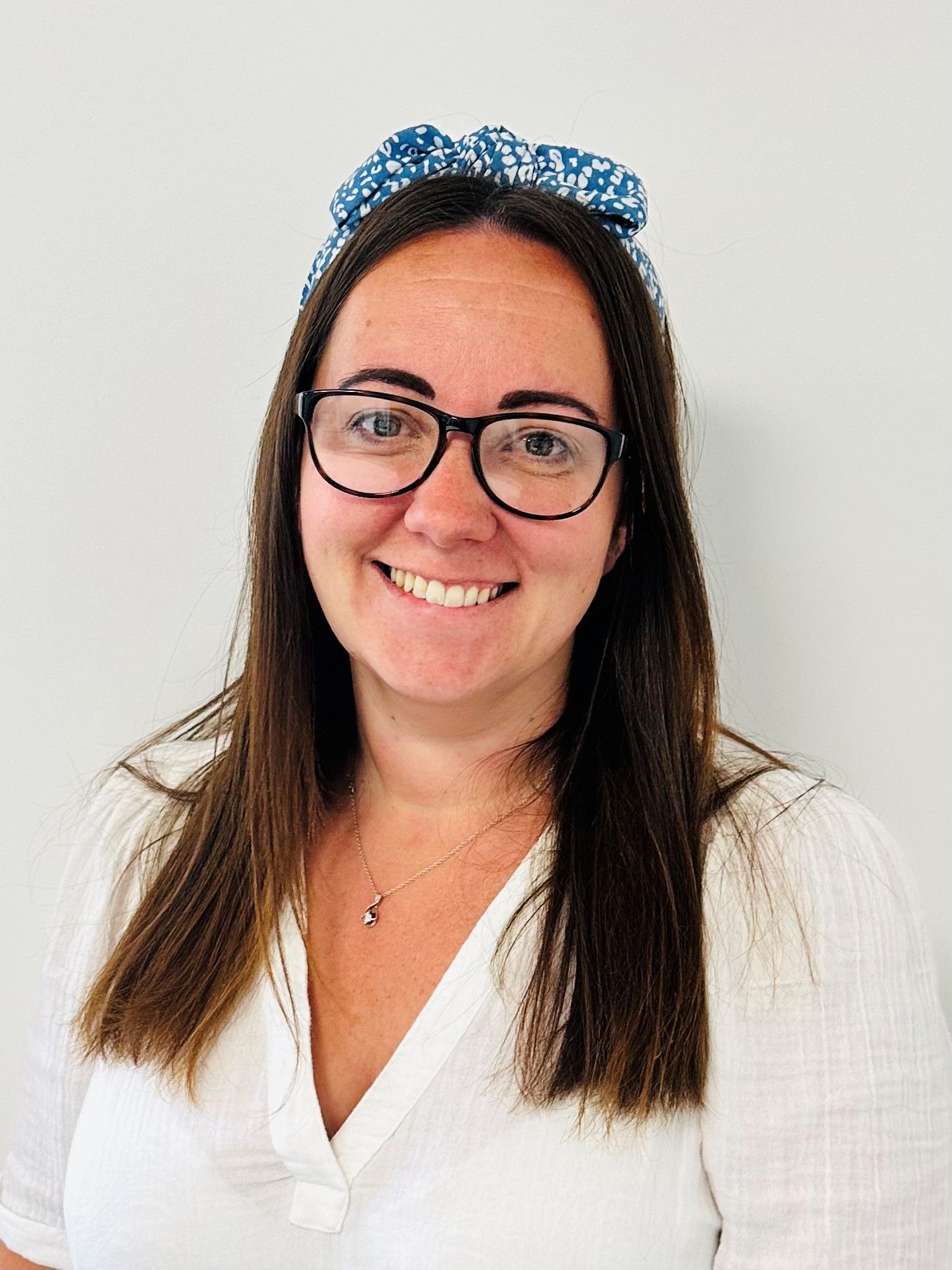 A woman wearing glasses and a headband is smiling for the camera.