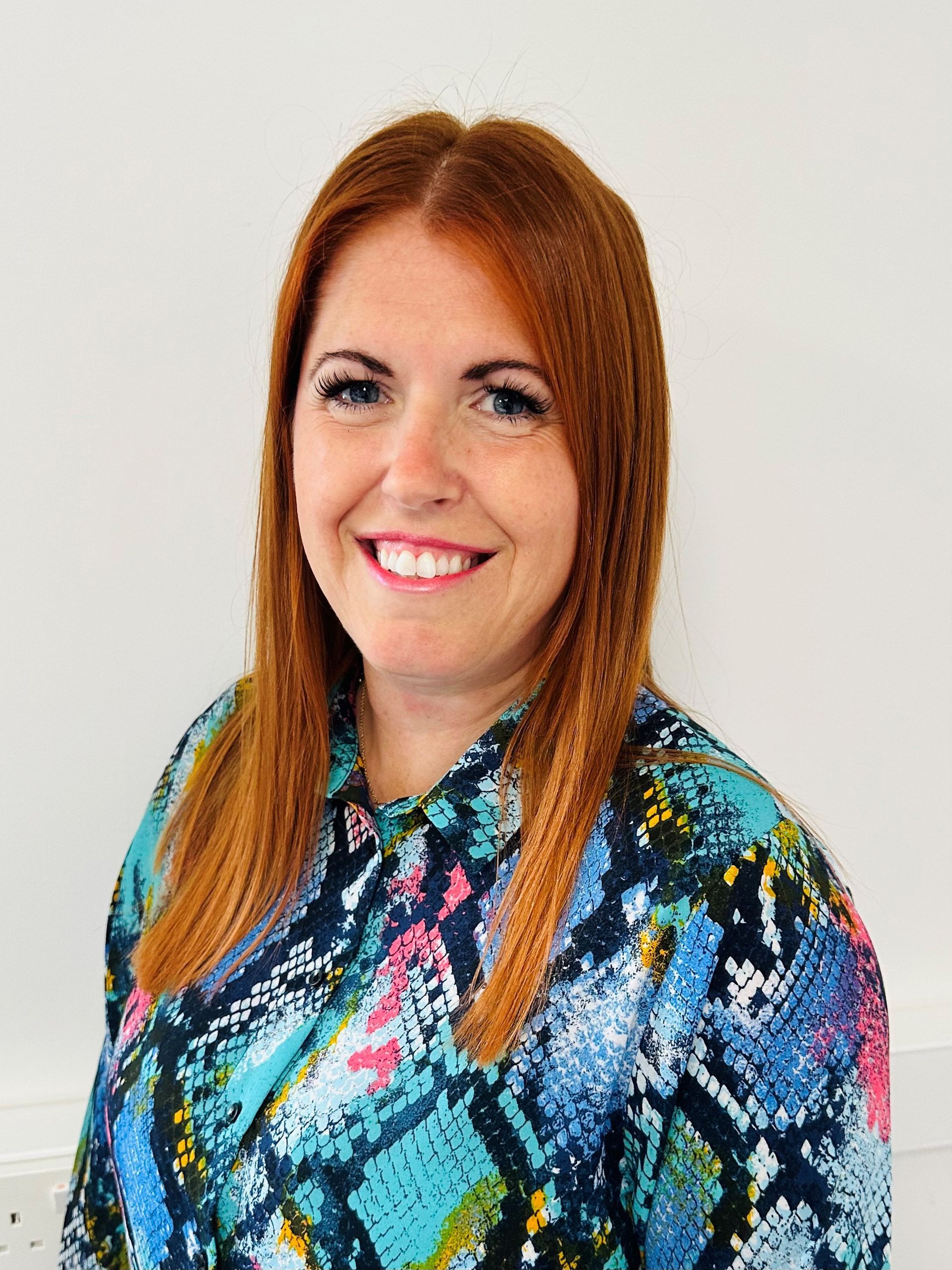 A woman with red hair is wearing a blue shirt and smiling.