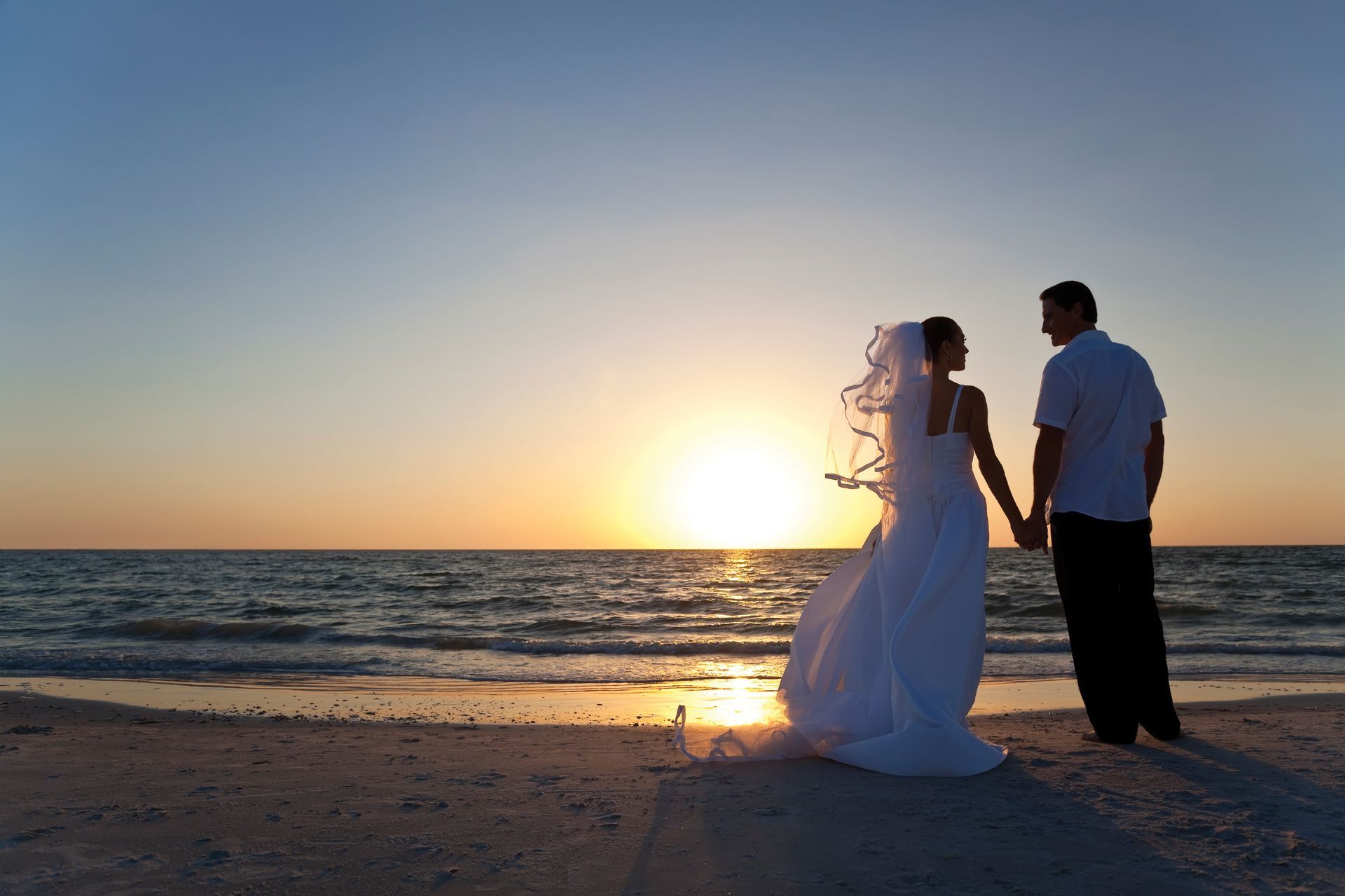Weddings A bride and groom holding hands on the beach at sunset
