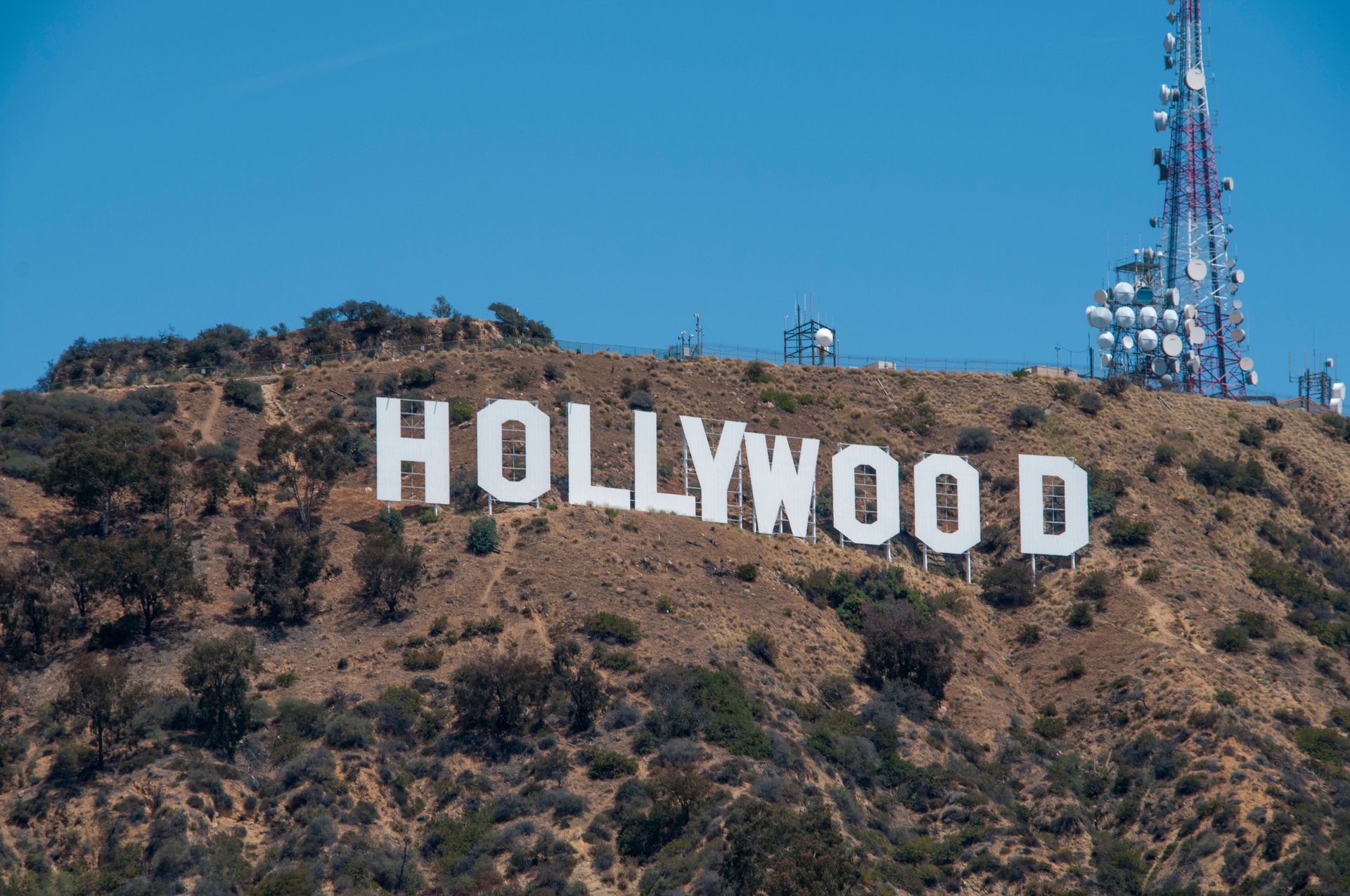 Hollywood sign on a brown hillside under a clear blue sky, with a communications tower nearby.