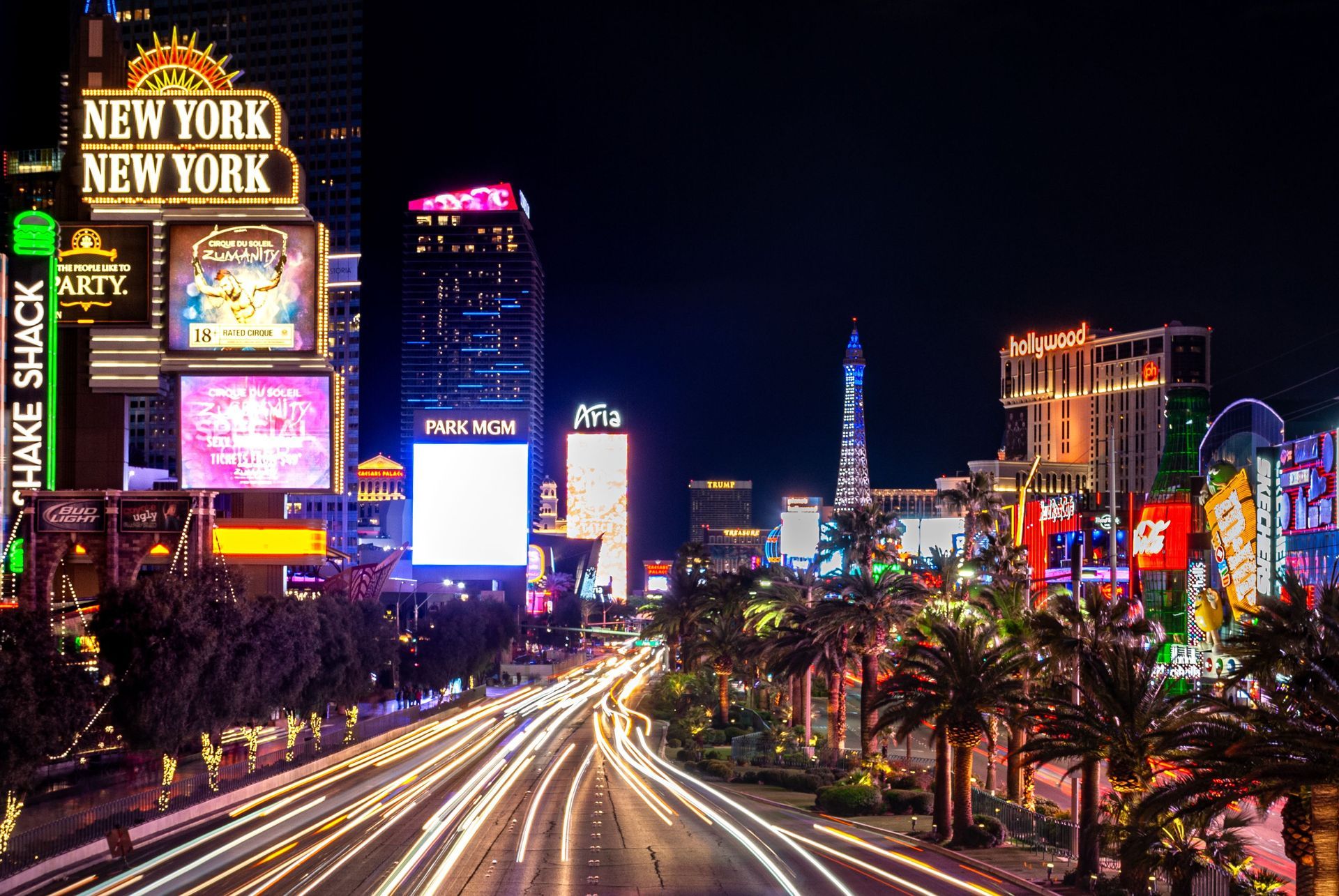 Las Vegas Strip at night with bright neon signs, palm trees, and light trails from traffic
