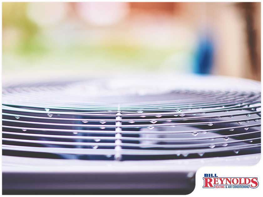 Close-up of an AC unit with water droplets on the metal fins, with a blurred background.