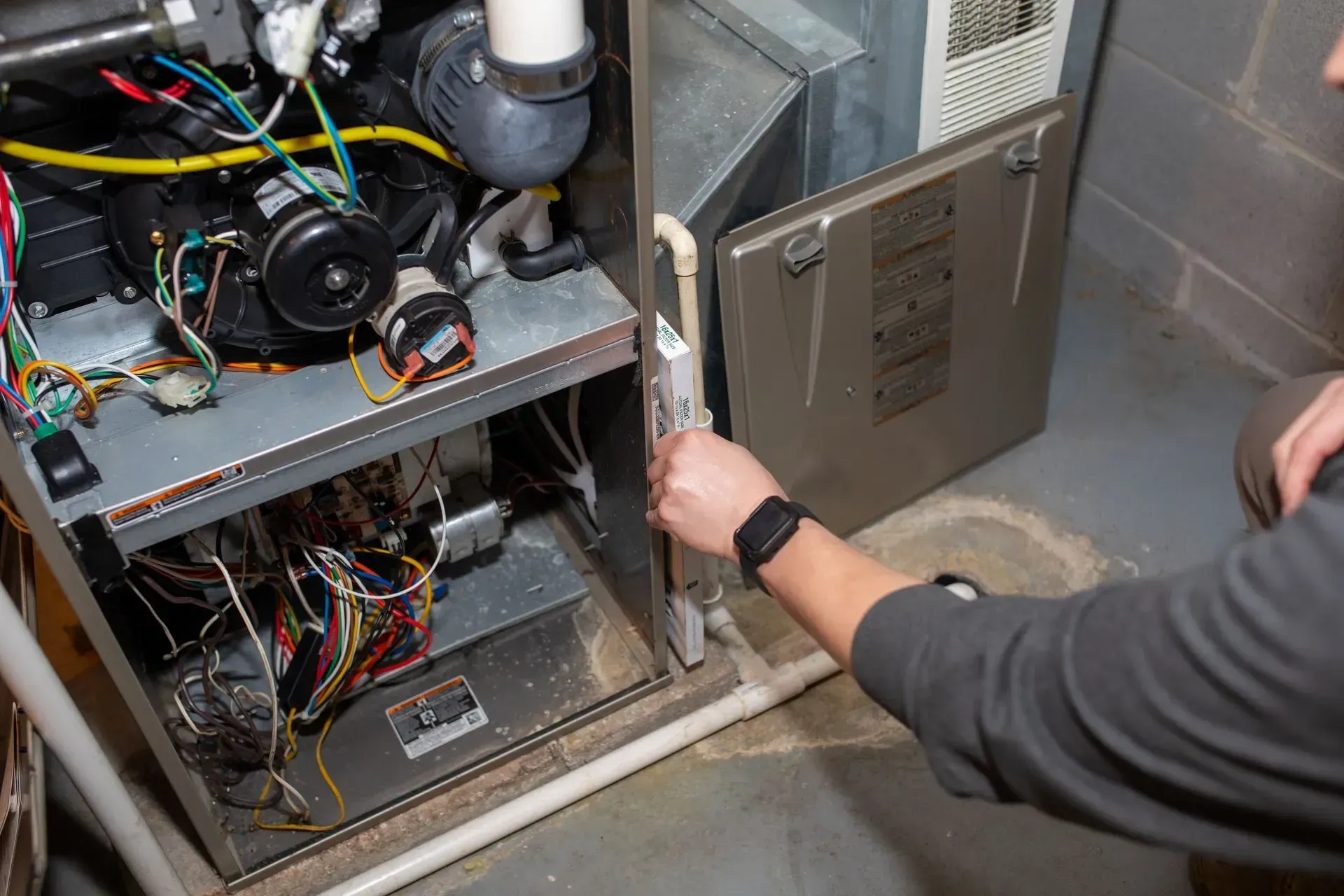 Person opening a furnace door in a basement, inspecting the internal components.