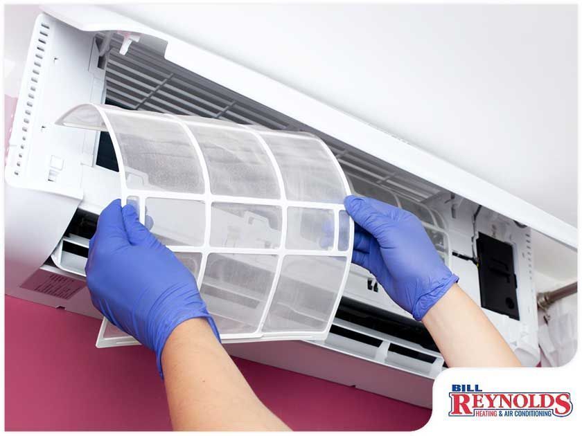 Person wearing blue gloves removing an air filter from an air conditioning unit.