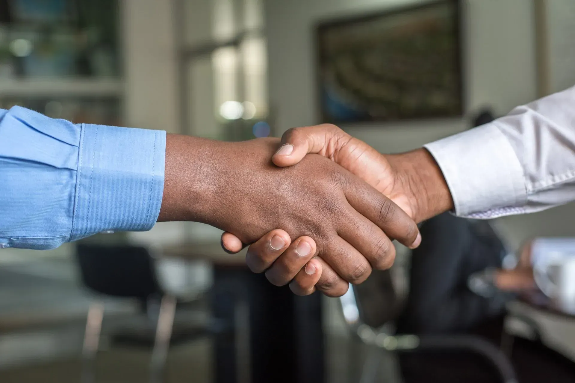 Two people shaking hands, a business deal in an office setting. Blue and white sleeves visible.