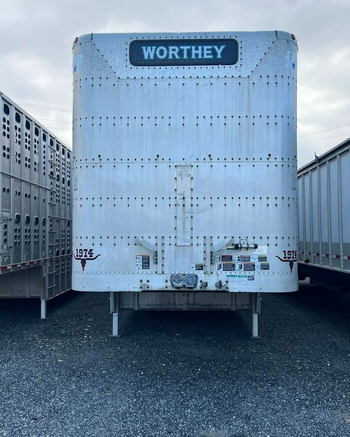 White WORTHY refrigerated trailer viewed from the rear in a gravel lot, flanked by other trailers.