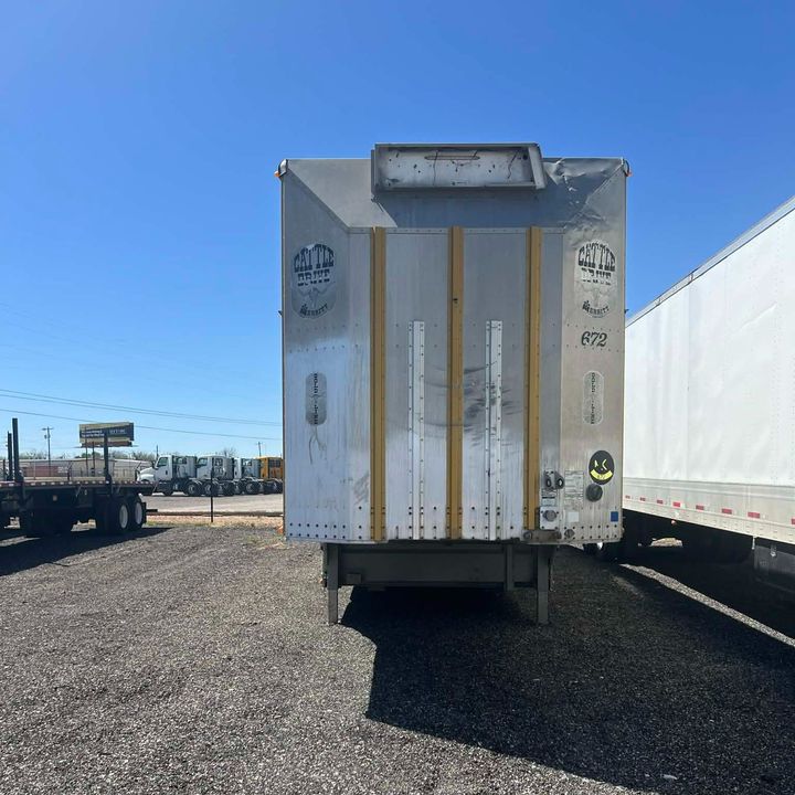 Rear view of a white refrigerated semi-trailer parked on a gravel lot under a blue sky