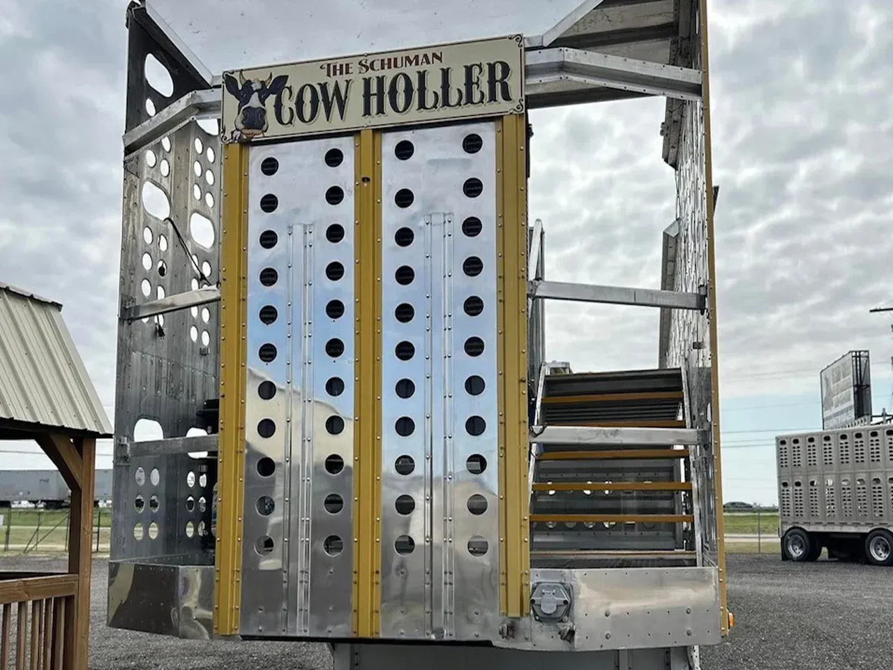Tall silver climbing wall with black handholds and a “COW HOLLOW” sign at an outdoor fairground
