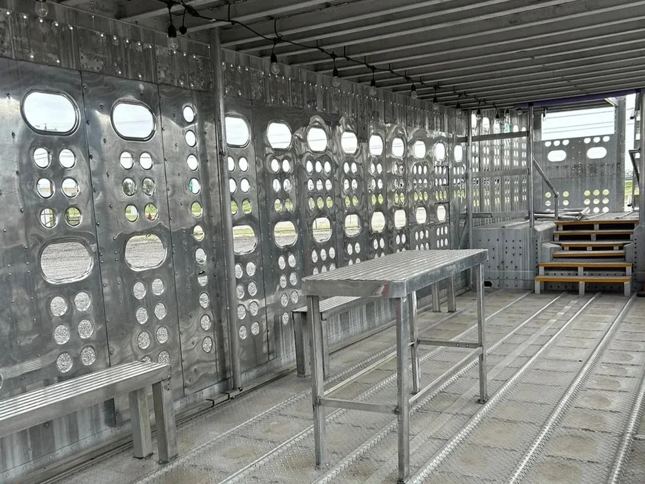 Empty industrial room with metal walls, tables, and stacked wooden pallets near a stairway