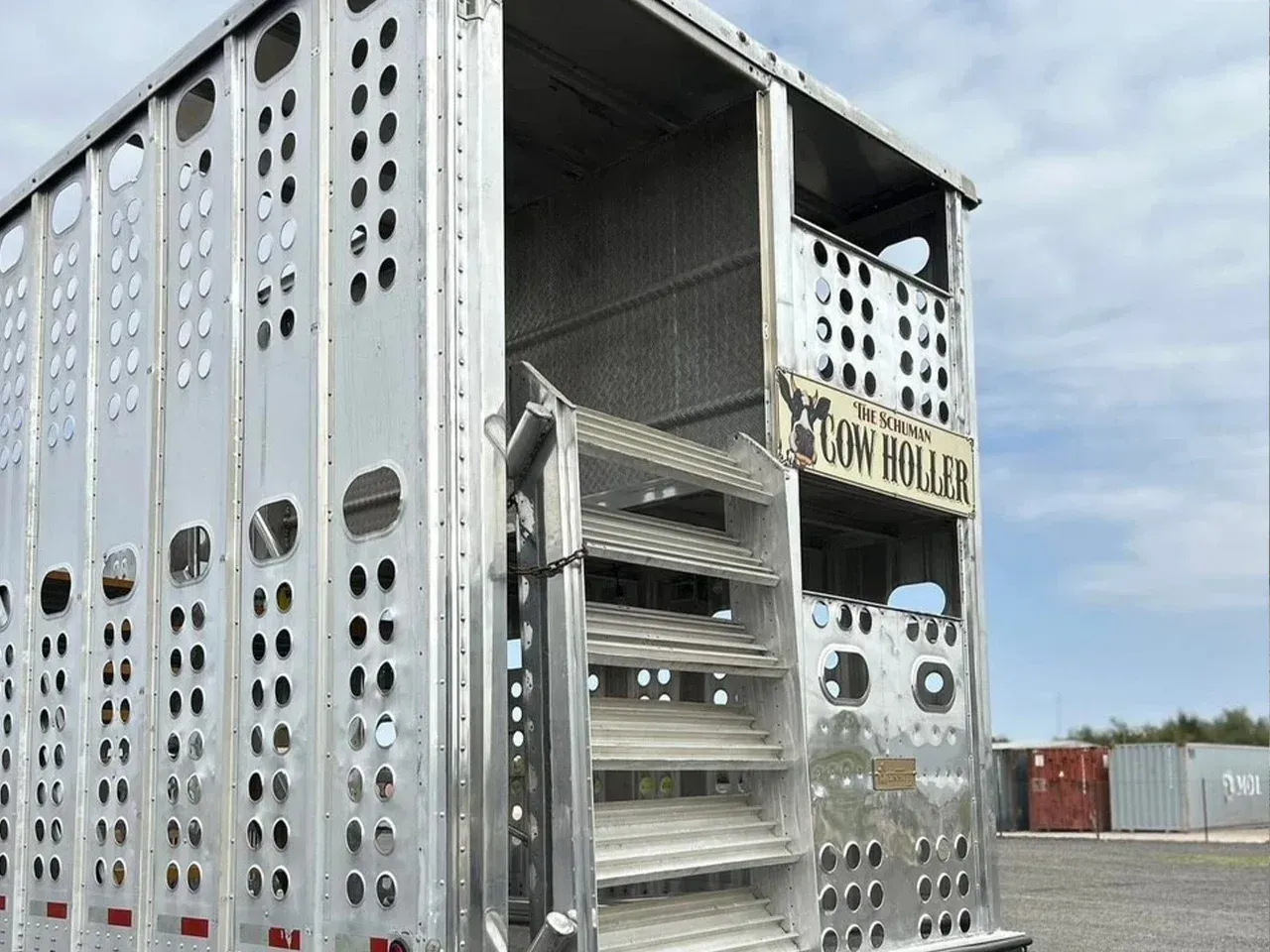 Silver livestock trailer with open back doors and stacked metal ramps in an outdoor lot