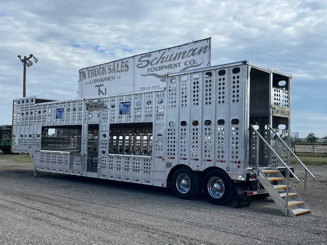 White multi-level trailer with ramps and signs, parked on gravel at an outdoor lot.