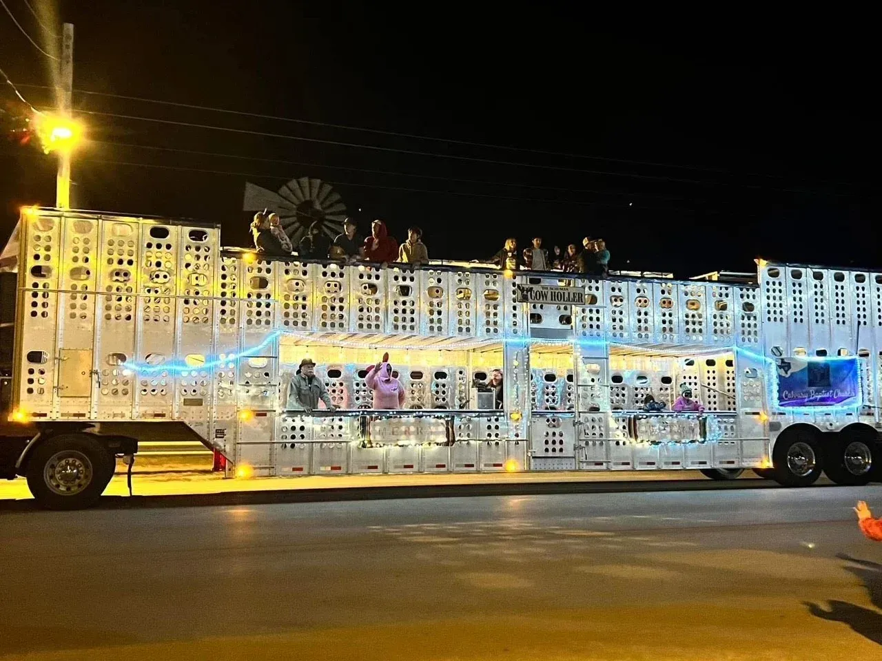 Illuminated white parade float bus with people inside, parked at night on a street